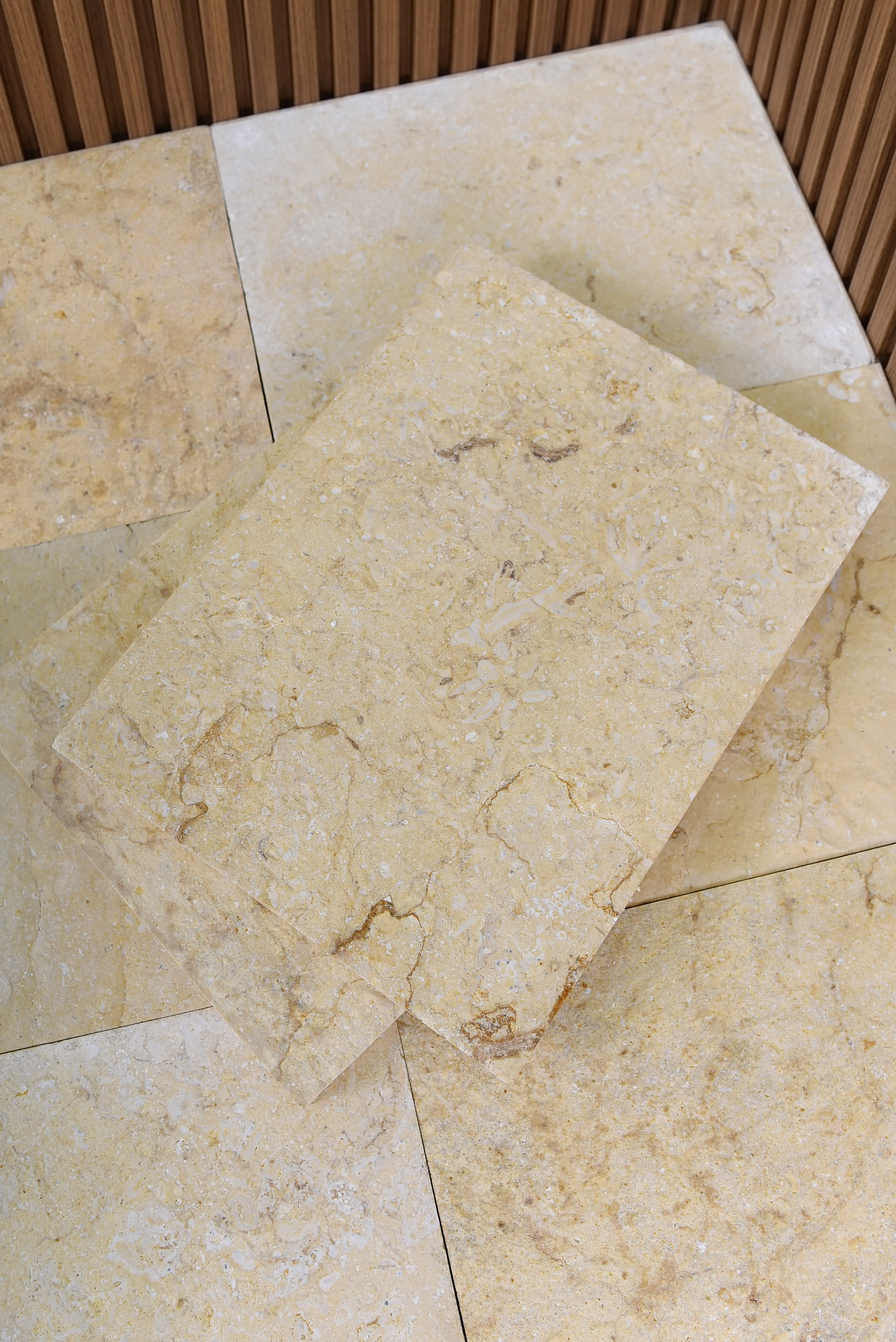 Light colored stone tiles background Close-up view of light beige travertine stone tiles with natural veining and fossil inclusions, an example for how to evaluate marble suppliers.