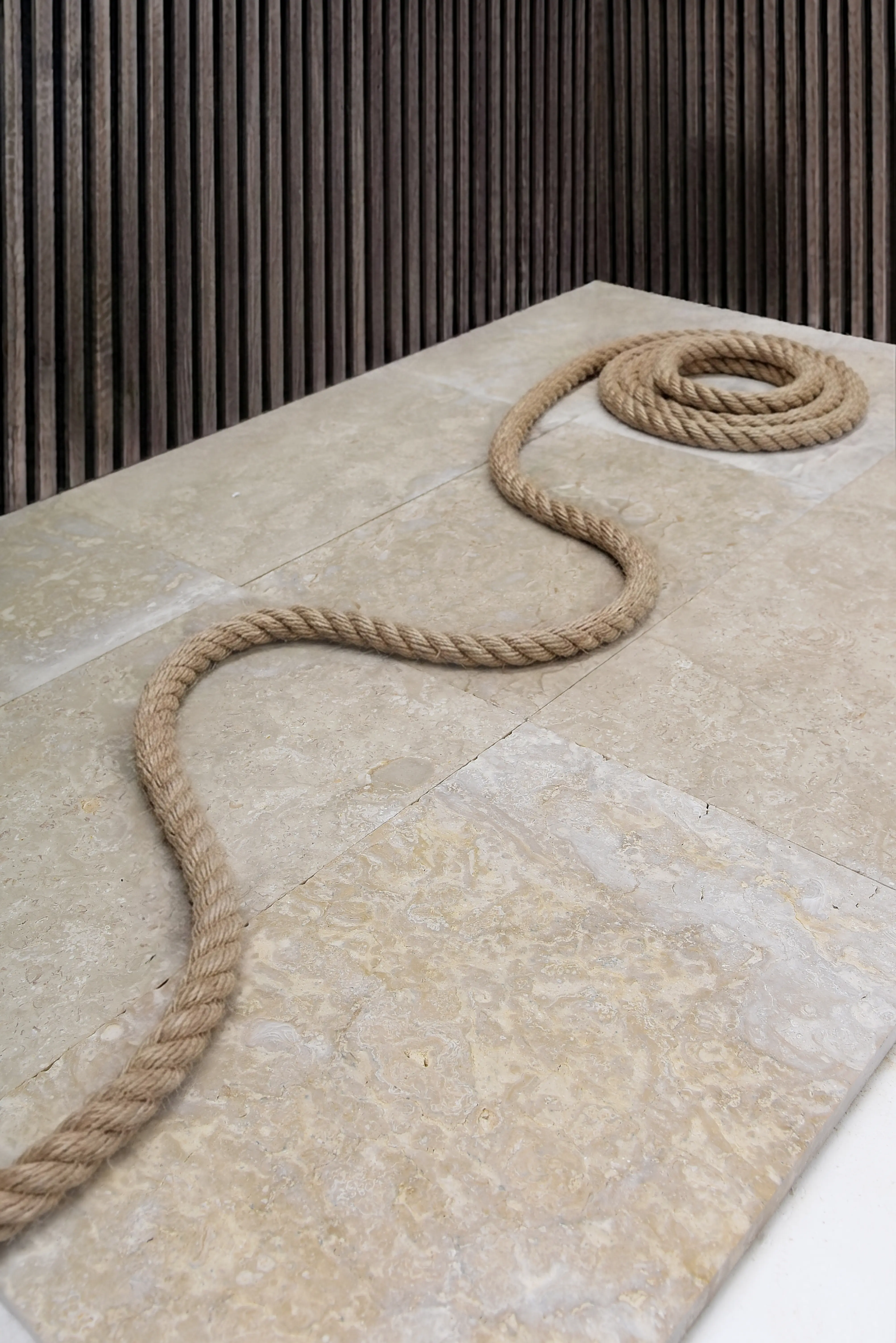A thick natural fiber rope coiled on a light-colored travertine stone surface, an example for types of masonry stone.