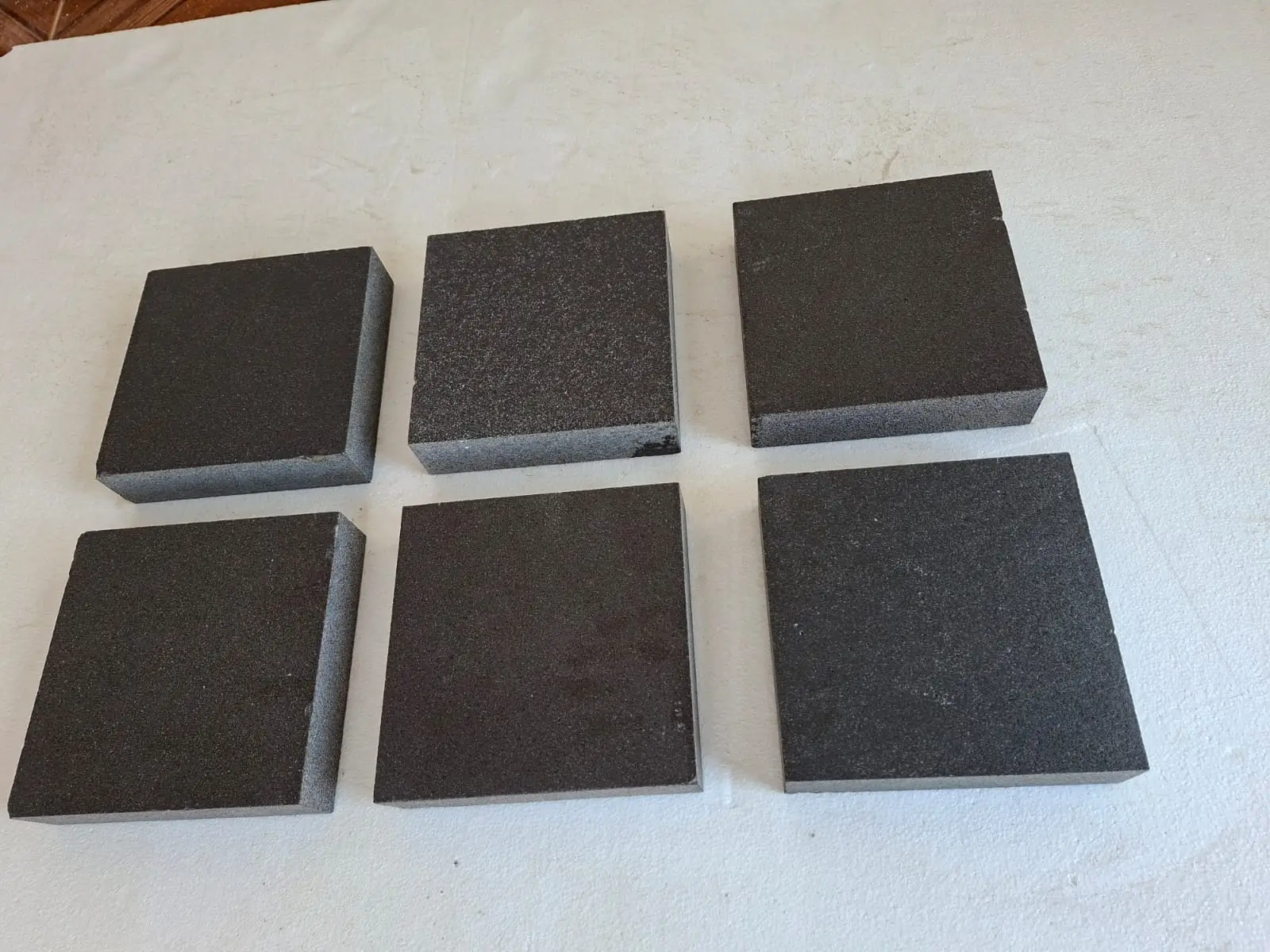 Six dark square stone samples Six dark square granite pavers are neatly arranged on a white surface, shown for joint fill for cobblestone setts.