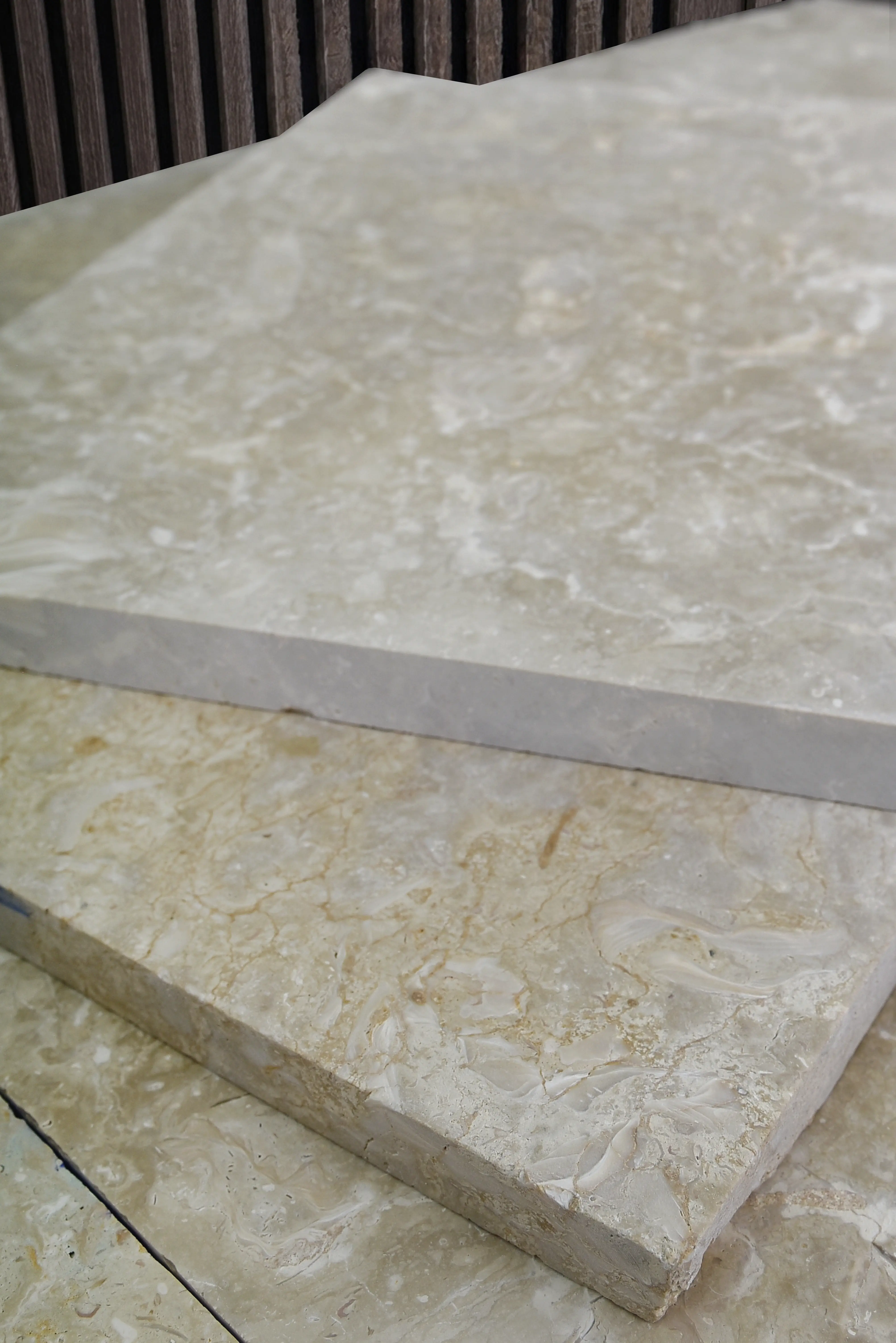 Cream-colored marble slabs with natural veining stacked, featuring a textured wood background, shown for types of landscaping rocks.
