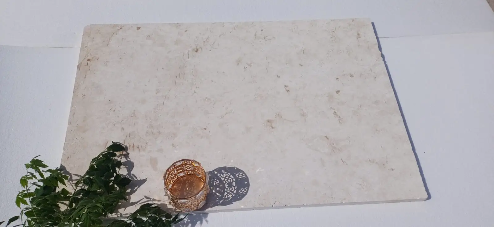 A textured limestone slab with a decorative gold candle holder and green vines, relevant to faux vs natural stone garden wall.