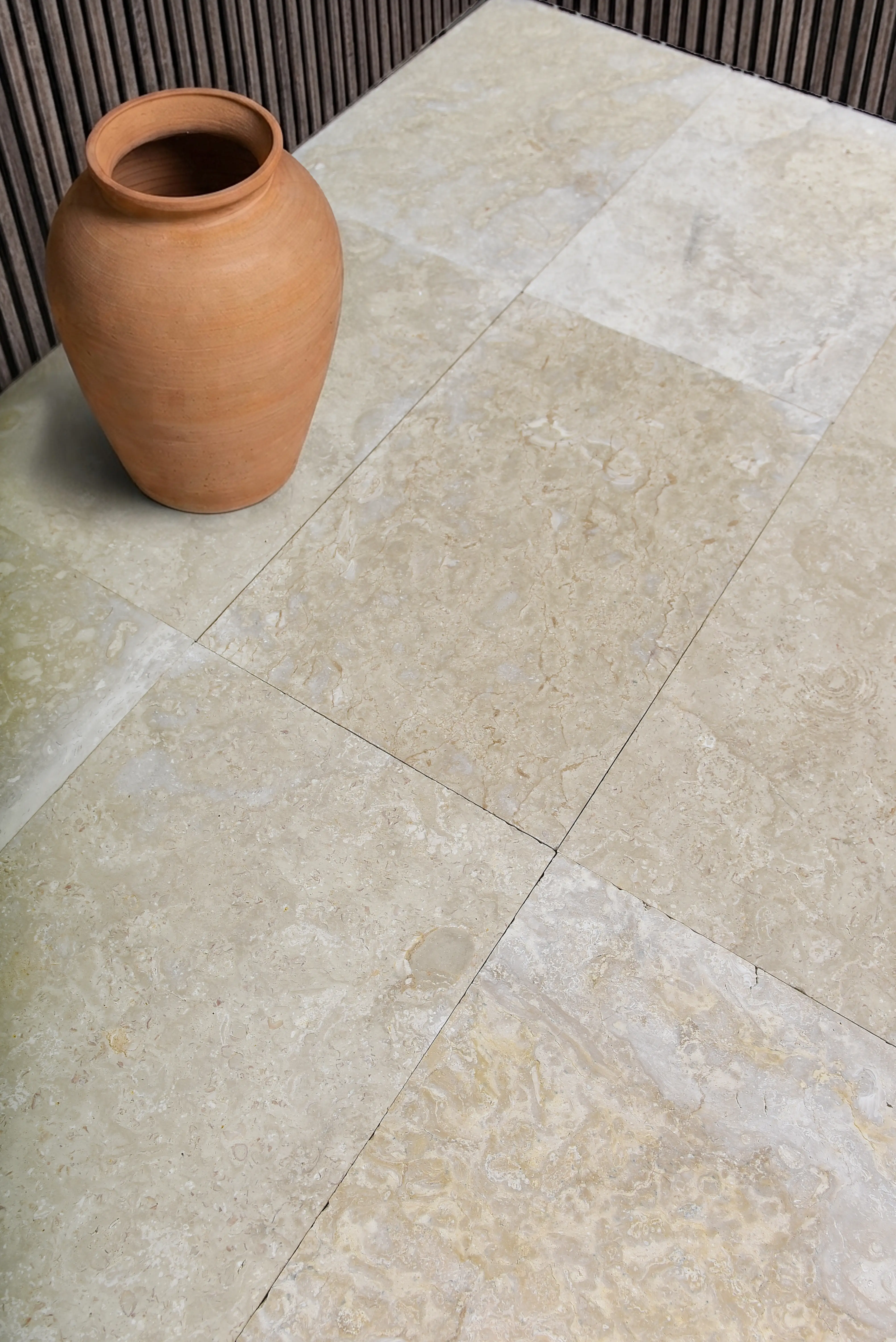 Terracotta Pot on Marble Floor A rustic terracotta pot rests on a textured travertine tile floor, an example for flagstone patio installation cost.