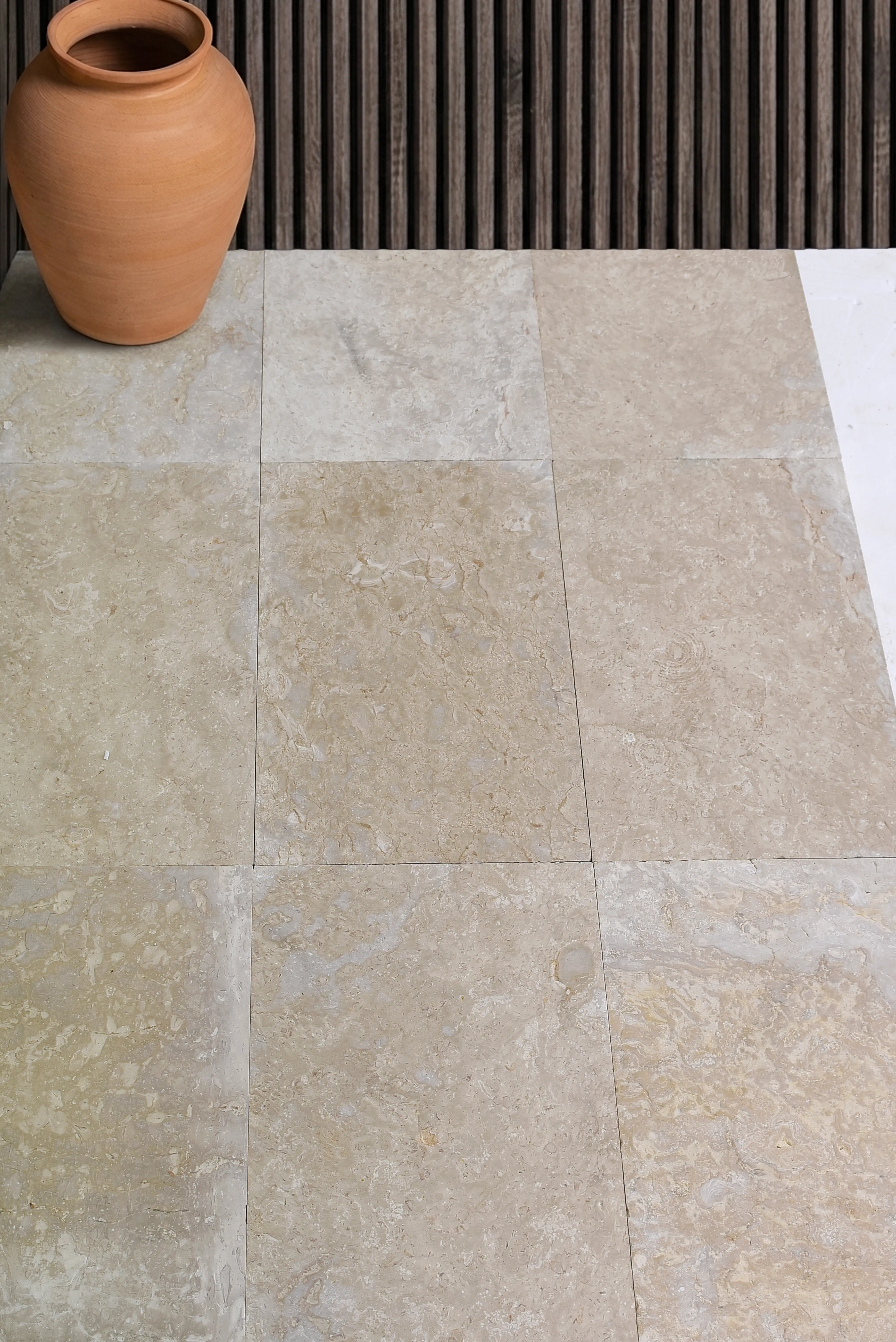 A large terracotta pot sits on natural stone tiles with a wooden slat background, relevant to flagstone vs bluestone paving.