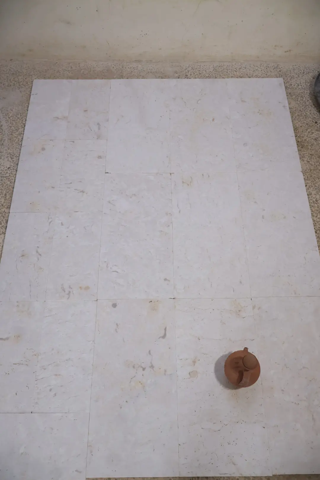 Small terracotta teapot on light beige stone pavers with subtle veining, pictured for how to install patio paver edging.