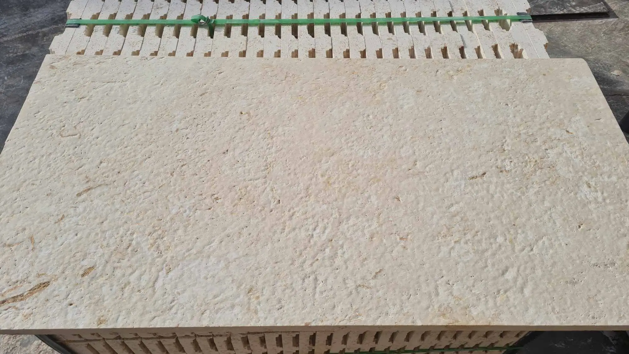 Close-up of rough textured beige limestone paving slabs stacked for display, shown for gray travertine pool coping.