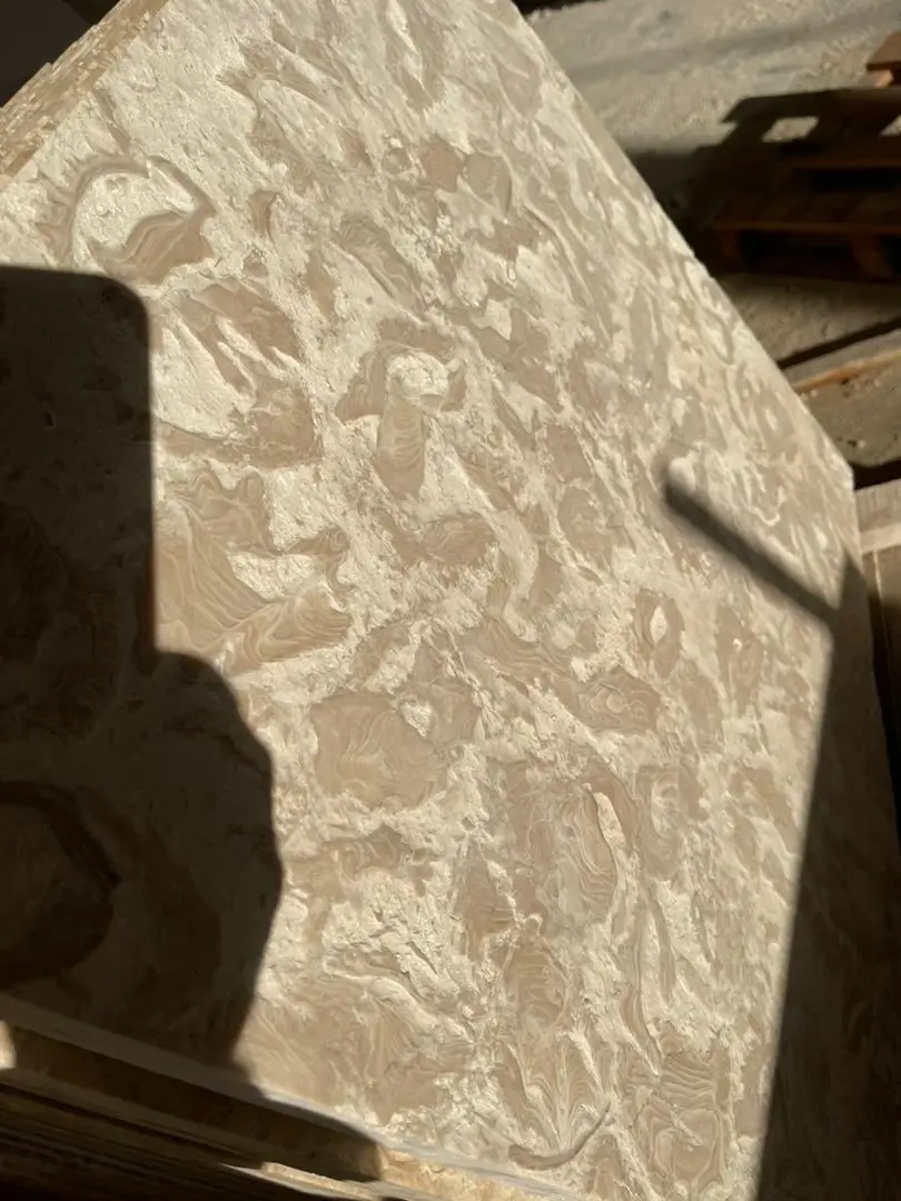 Close-up of a textured travertine slab surface with swirling beige and white patterns, shown for bluestone patio.