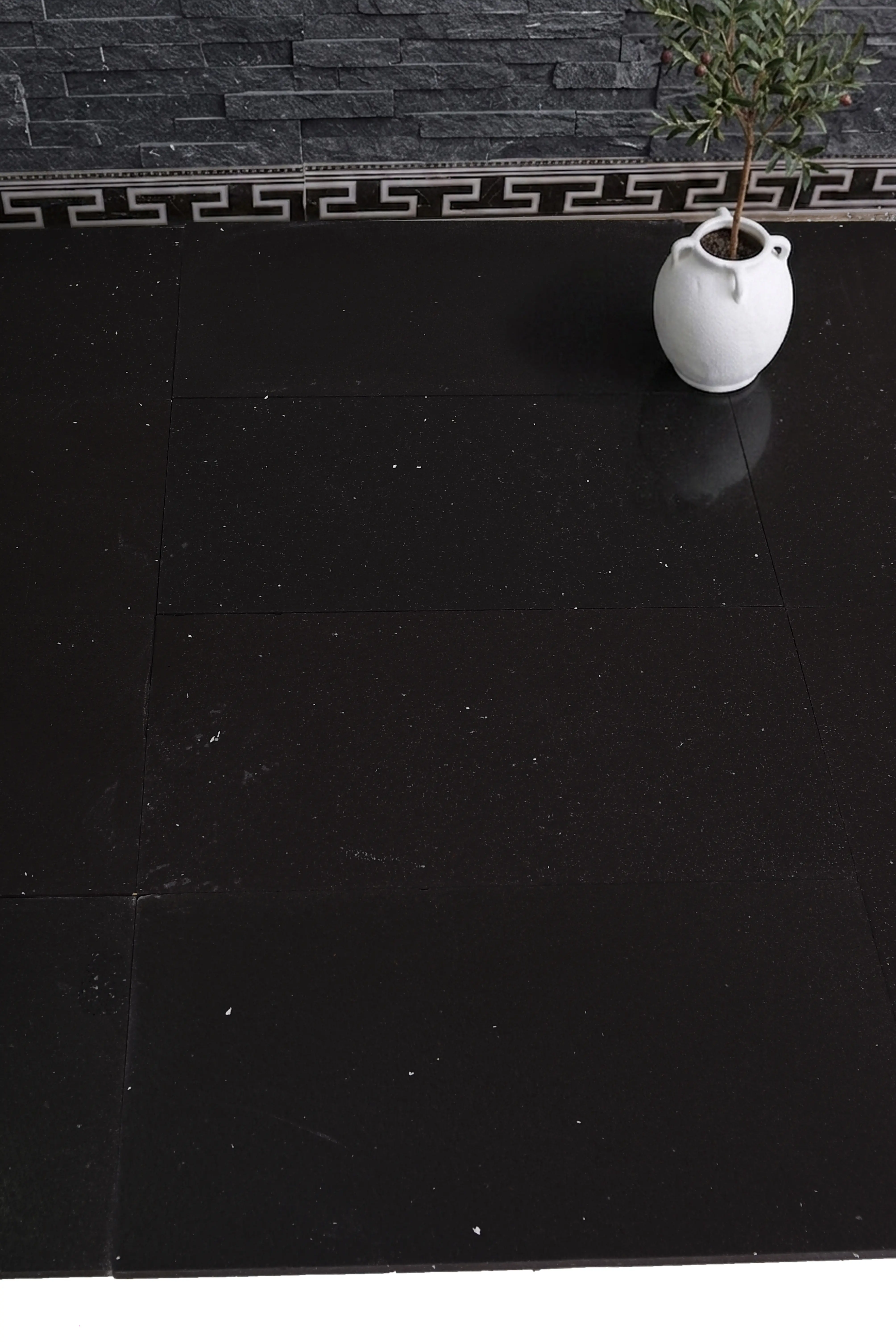 Close-up of polished black stone floor tiles with a decorative Greek key border, an example for grey limestone countertops.