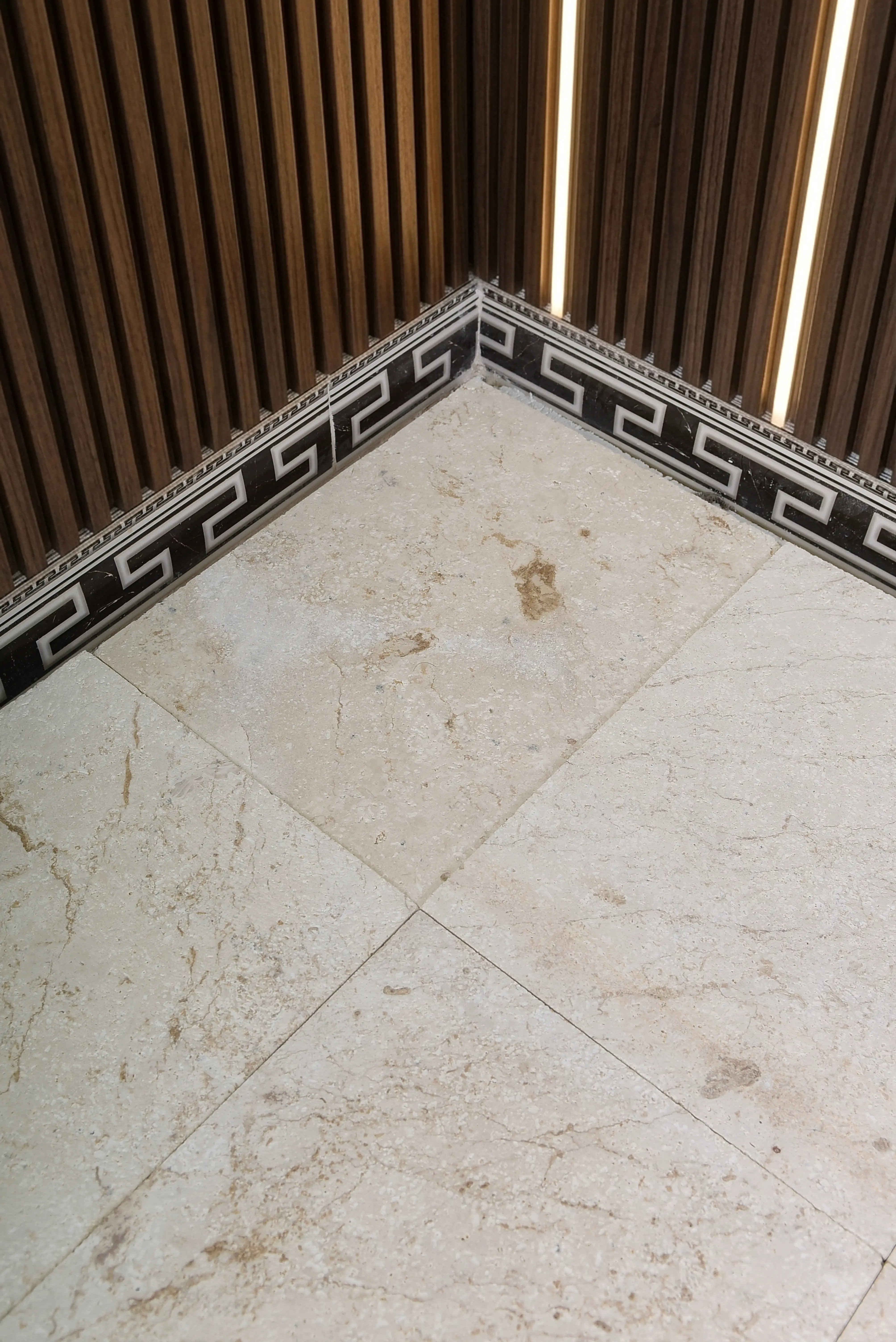 Elegant corner featuring marble floor tiles with a decorative Greek key border and wood paneling, shown for what type of rock is granite.