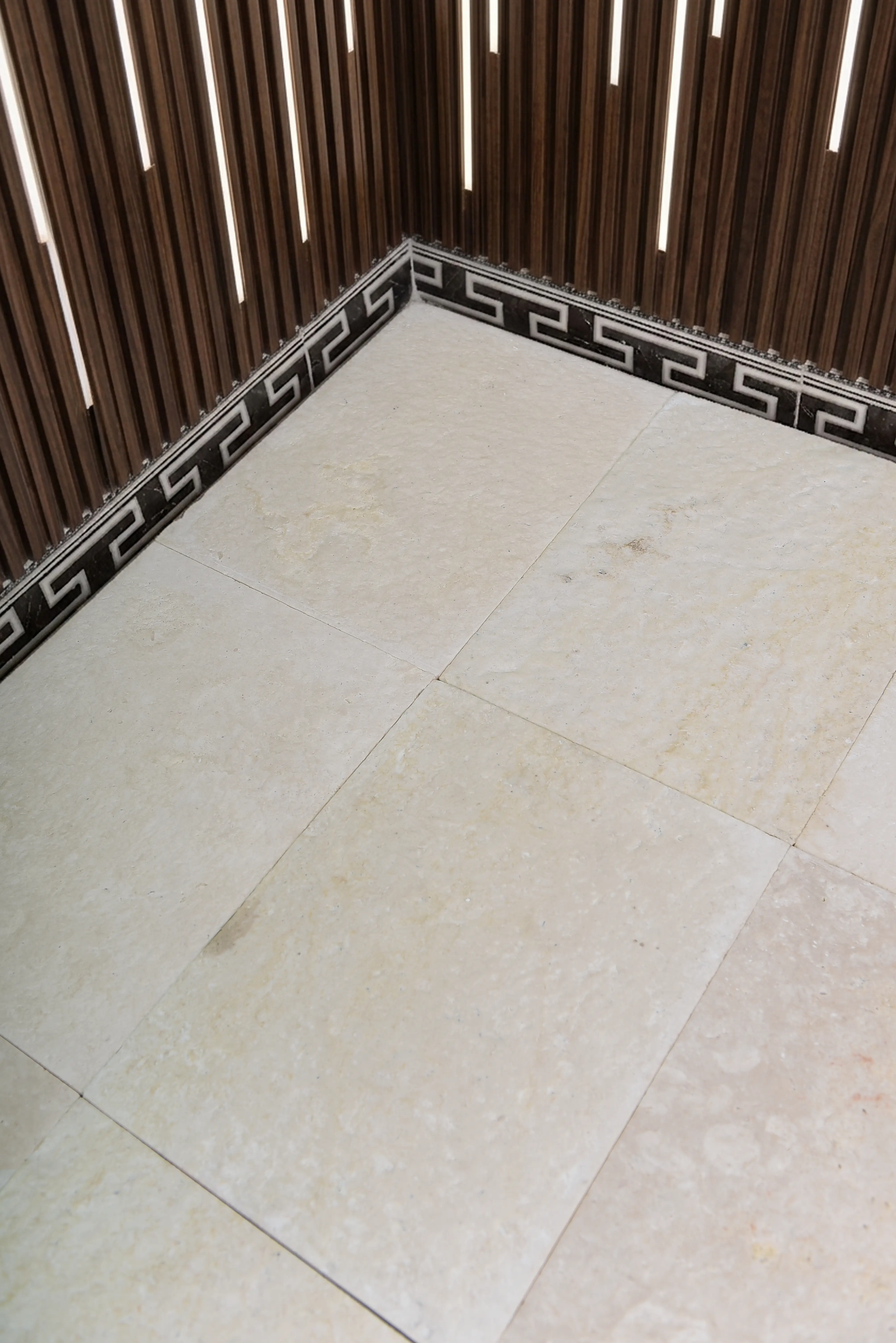 Cream marble floor tiles with a Greek key border accenting the corner, an example for Kerb Stones & Edging.
