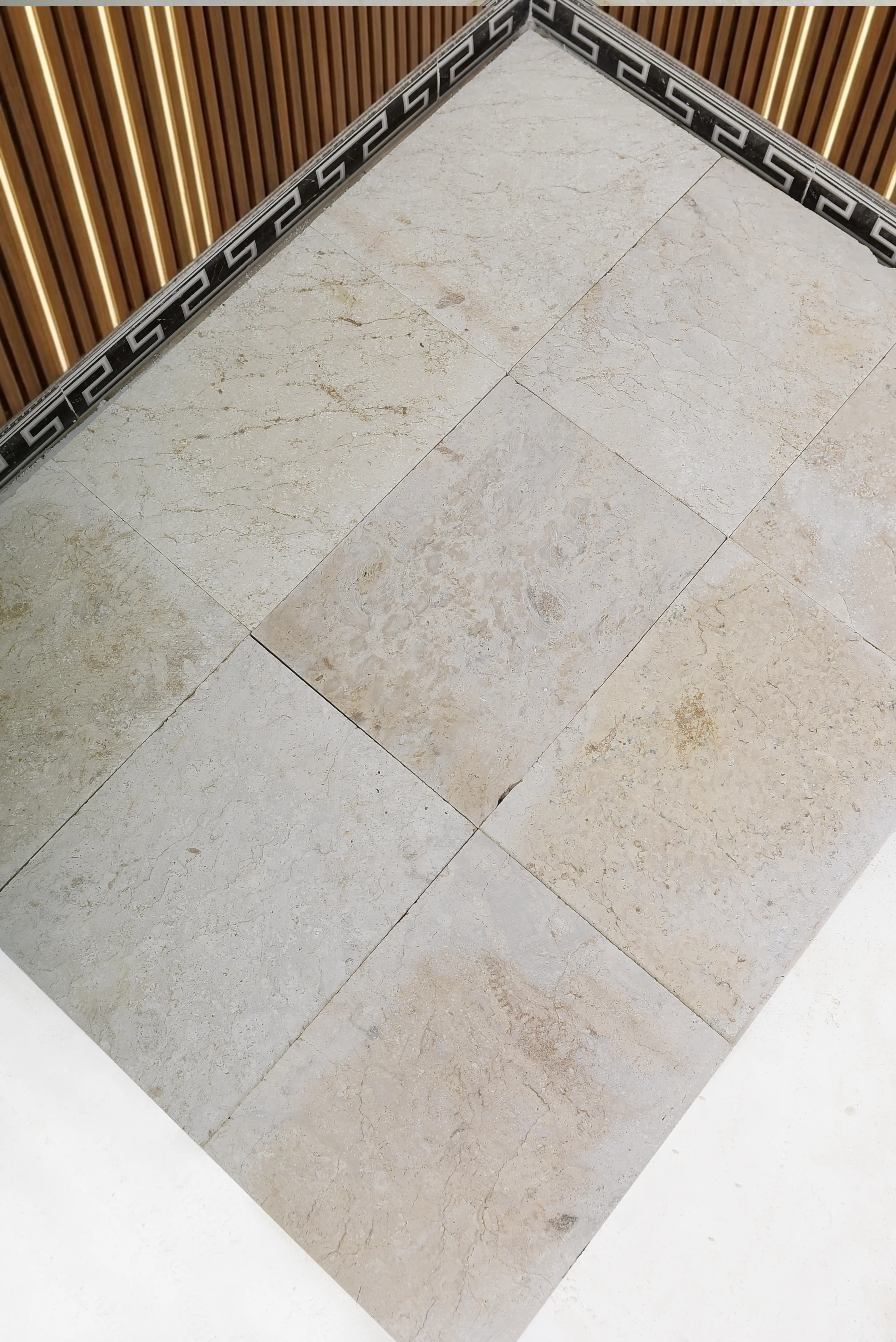 Corner of tiled floor and wood paneling Close-up of light beige marble floor tiles with a decorative border and wood paneling, a reference for landscape border wall stone problems.