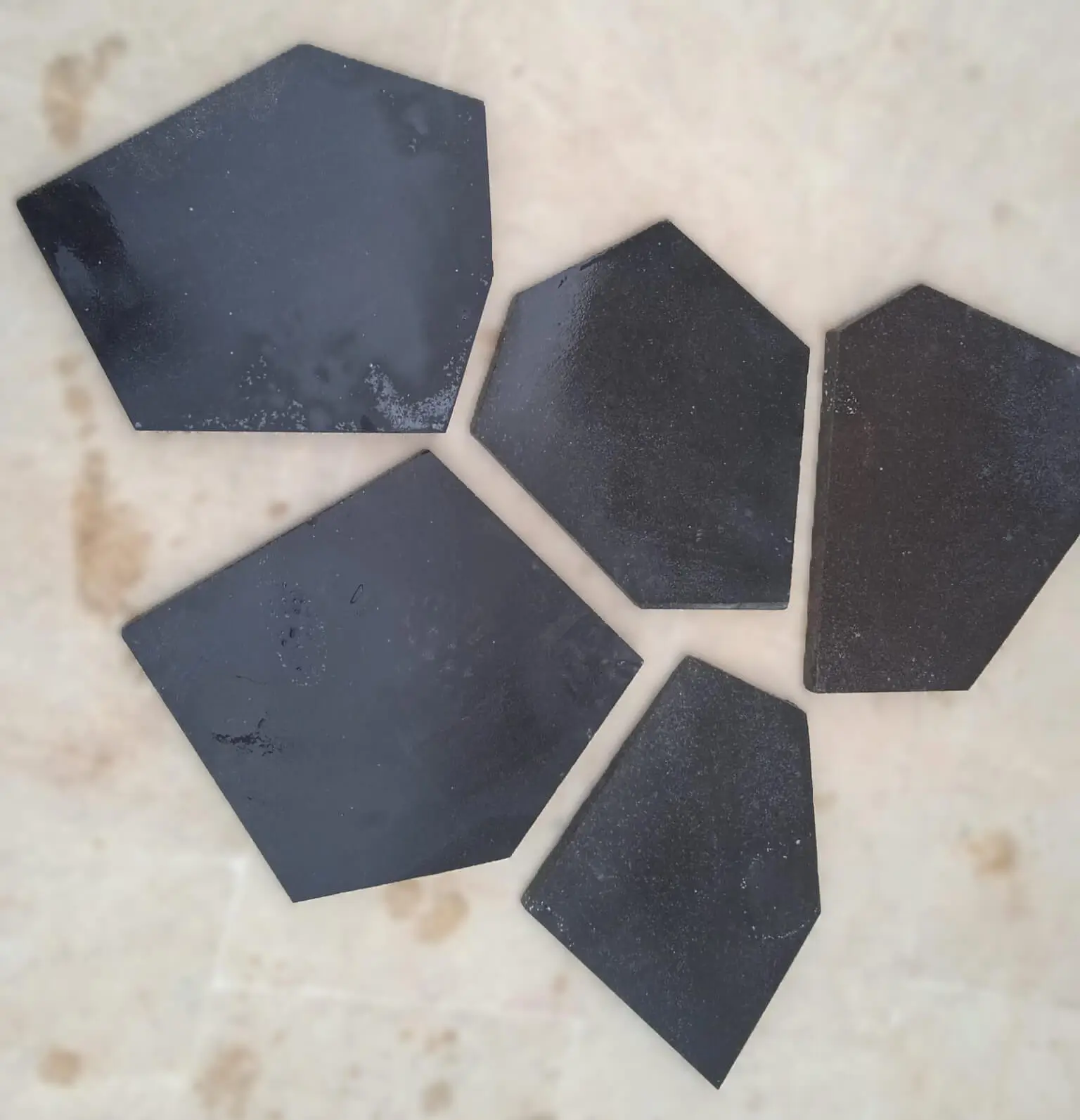 Dark Angular Stone Pieces Various dark, angular slate pieces scattered on a lightly textured surface, shown for keystone masonry.