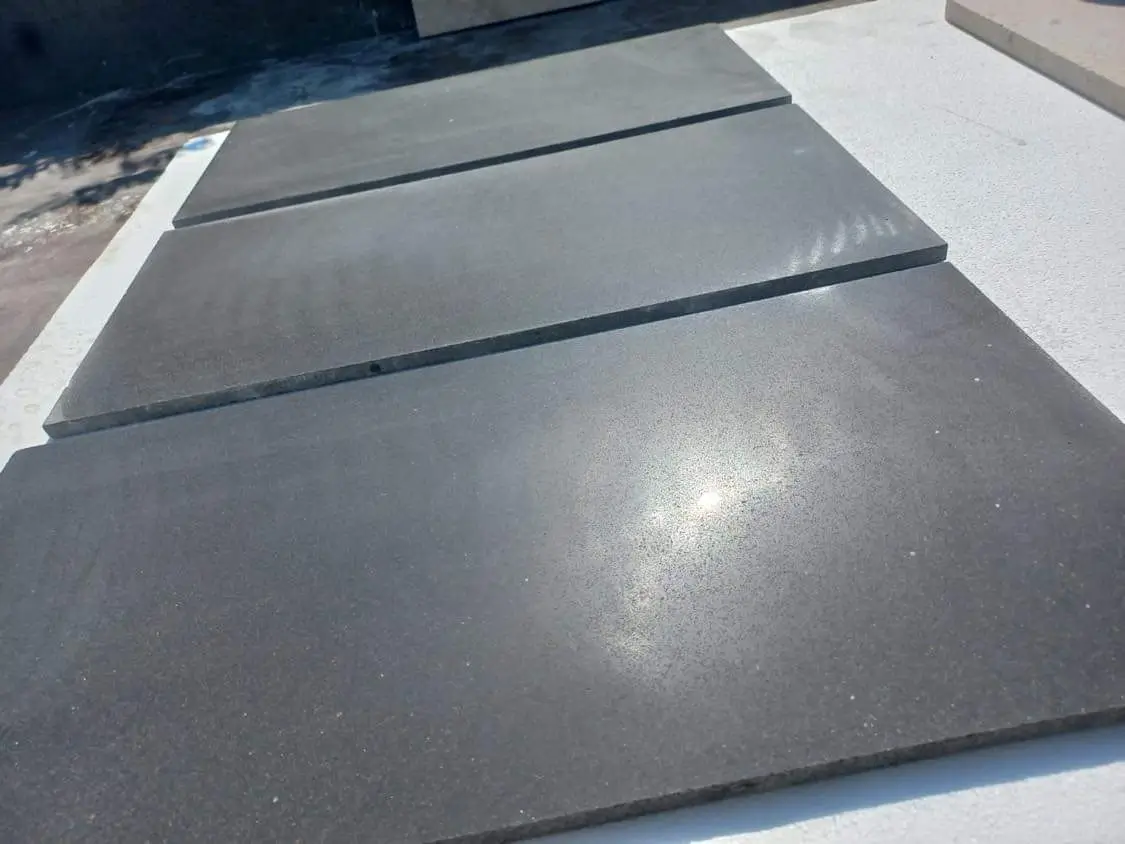 Dark slate slabs laid out in a row on a textured surface under bright sunlight, pictured for blue slate floor tile comparison.