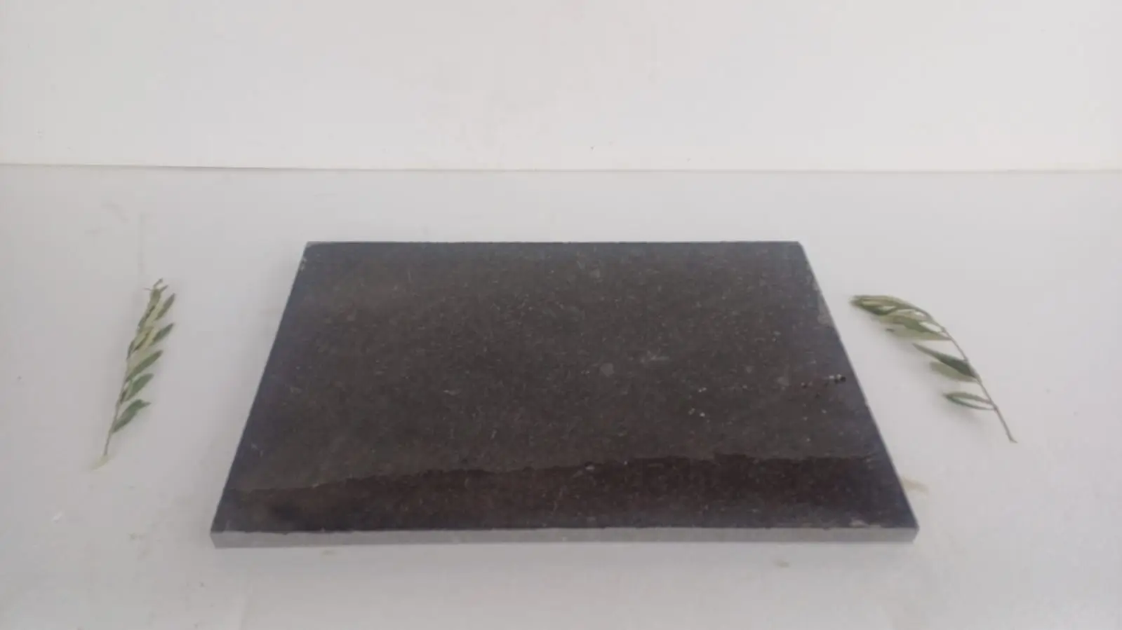Dark Stone Slab with Greenery A dark, rectangular stone slab is showcased with olive branches, highlighting limestone pavers, an example for natural limestone bathroom.