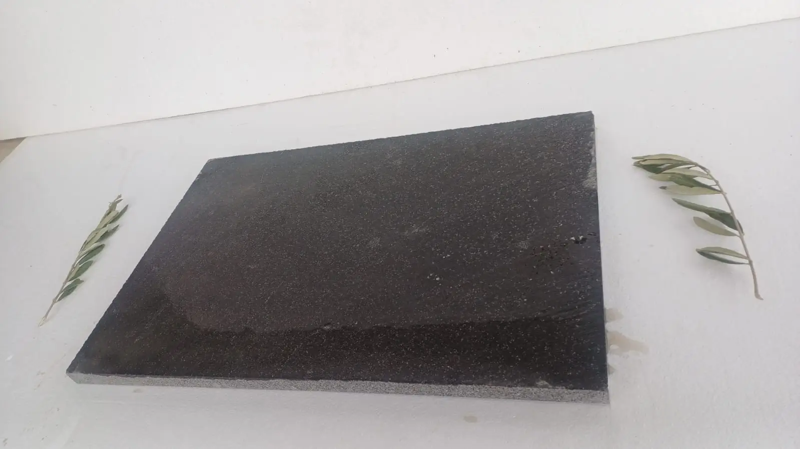 Dark Stone Slab with Olive Branches A dark granite slab is displayed with delicate olive branches on a white surface, relevant to how to seal flagstone.