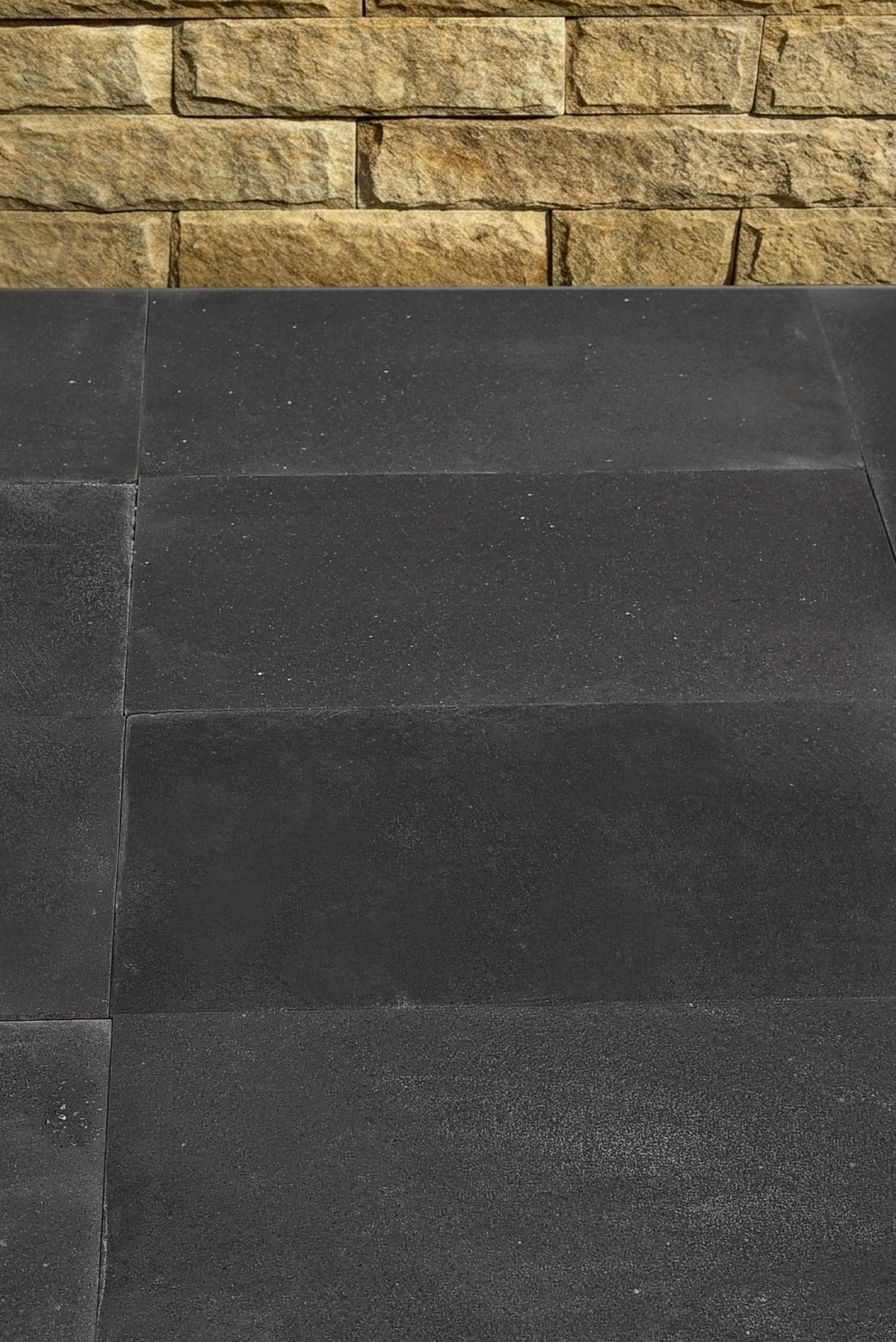 Dark Textured Pavers and Stone Wall Dark grey textured pavers contrast with a natural stacked stone wall above, relevant to reclaimed granite curb guide.
