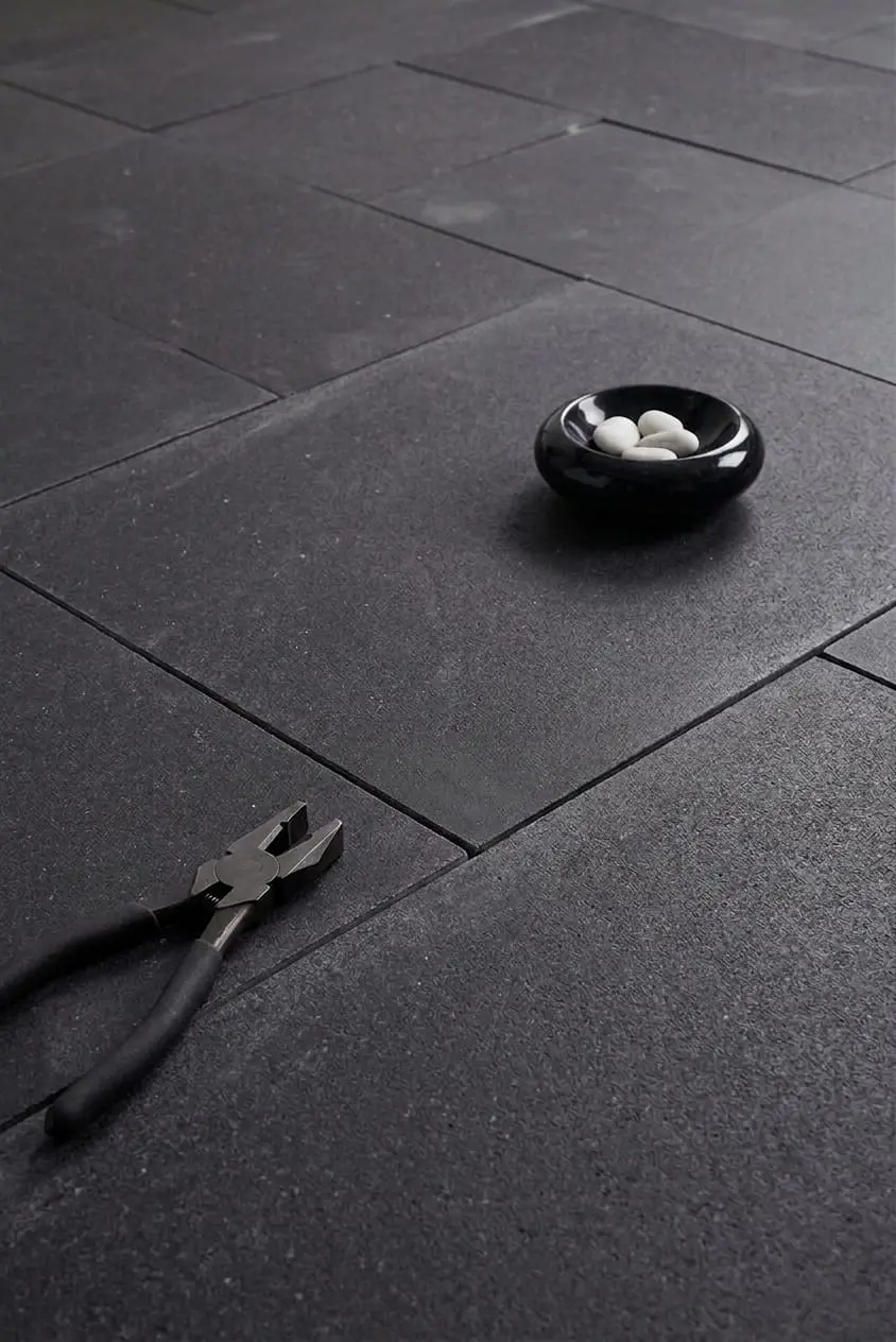 A pair of pliers and a small bowl of white stones on a dark textured surface, shown for belgian blue limestone flooring.