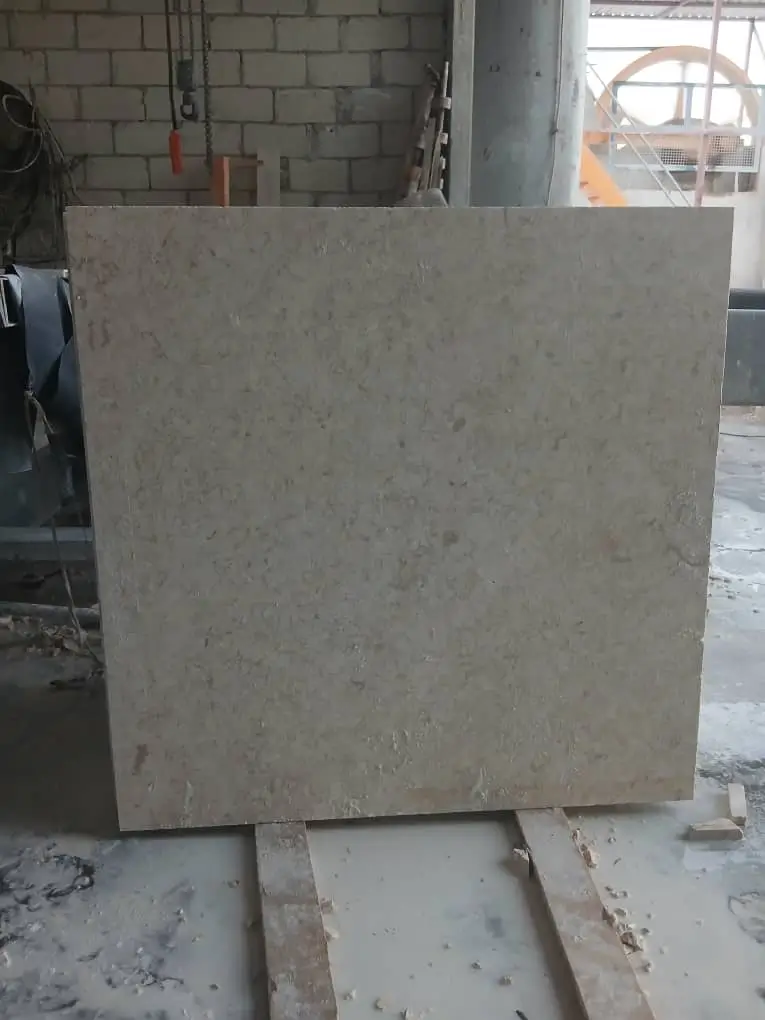 A large, light beige limestone slab with natural variations stands upright on wooden supports, relevant to ancient stone masonry techniques.