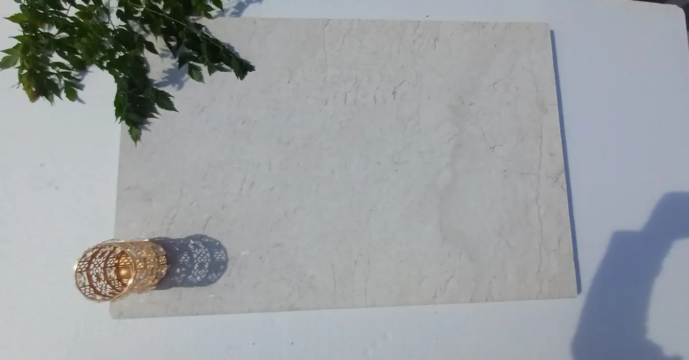 Close-up texture of a light beige marble slab with subtle veining and a decorative gold candle holder, relevant to what type of stone is travertine.