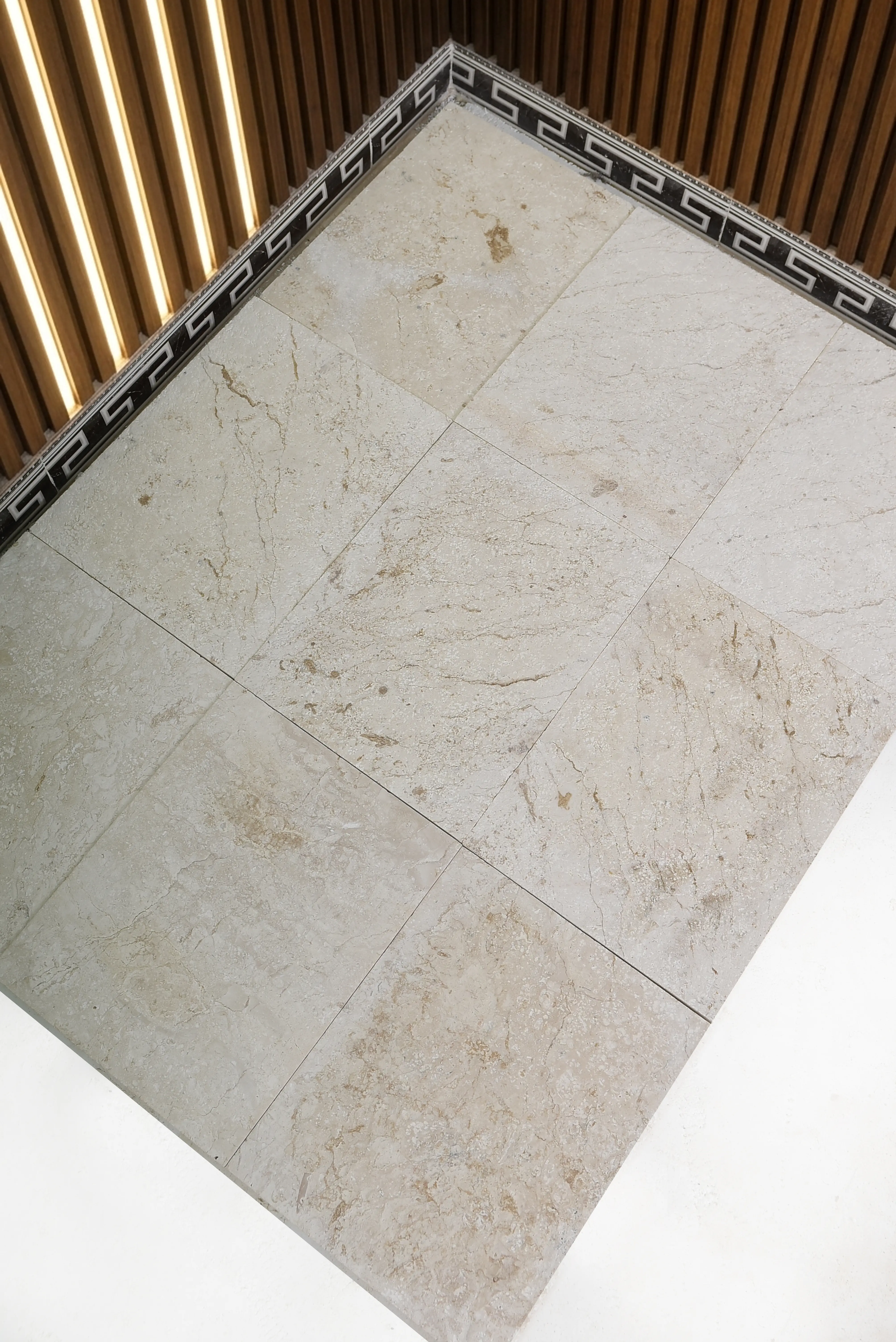 Close-up of polished travertine floor tiles meeting a decorative border and wood ceiling, shown for cheapest paving stones.