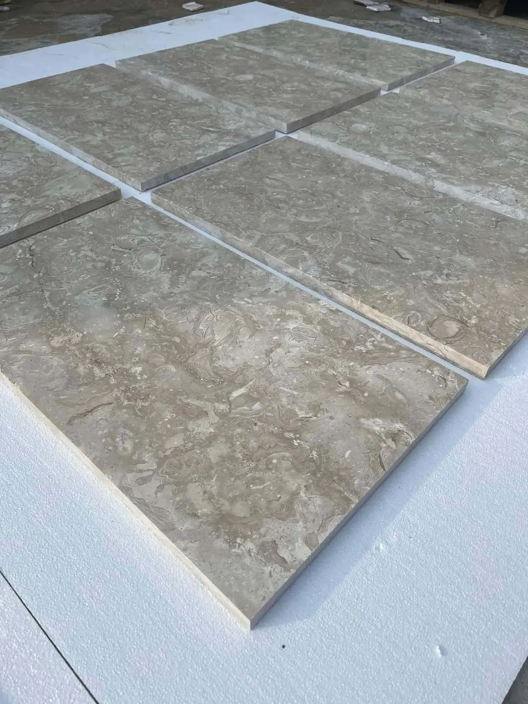 Beige limestone tiles with natural swirling patterns arranged on a white surface, a reference for yorkshire stone slabs for sale.