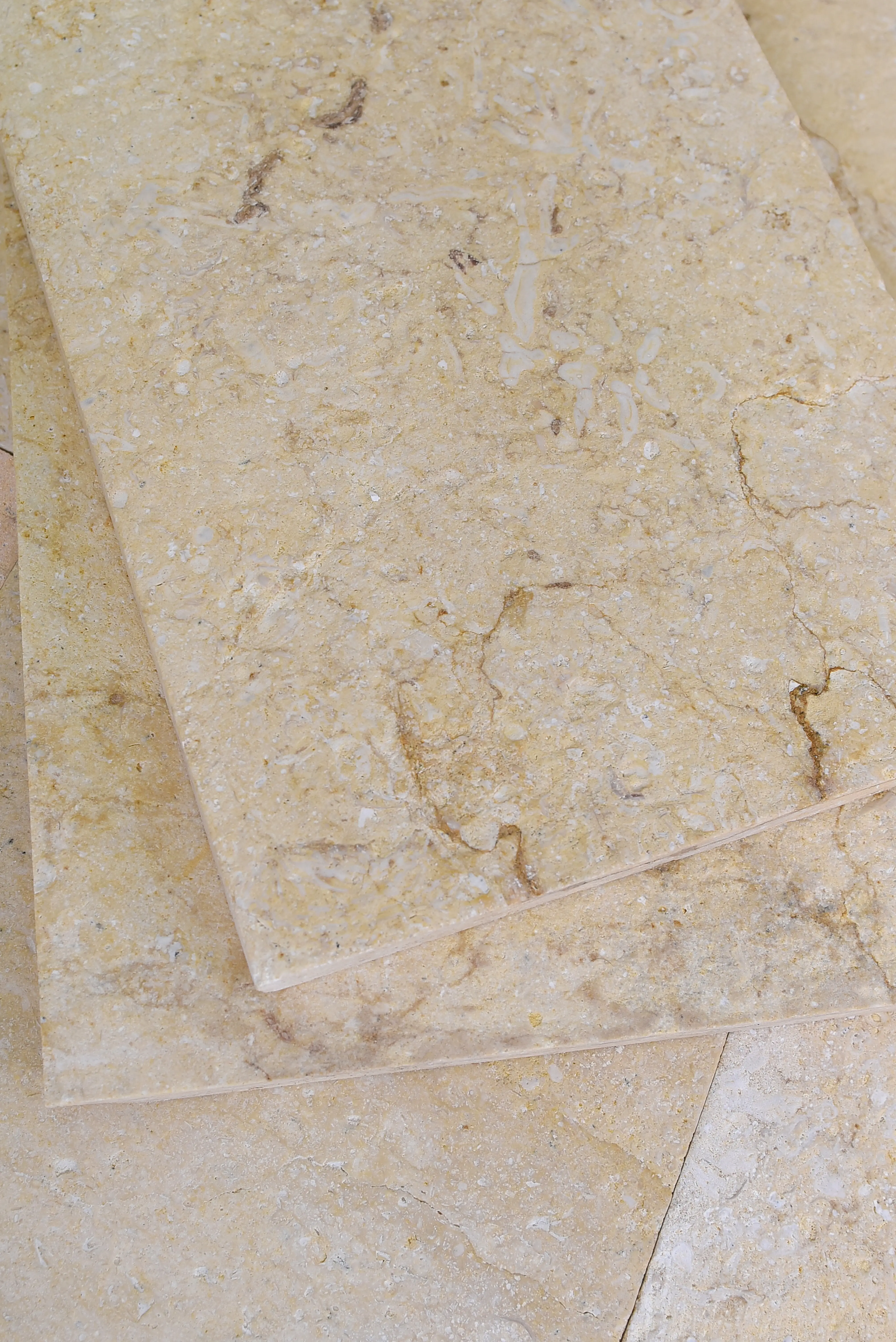 Close-up of stacked beige marble tiles with subtle brown veining and texture, an example for blue stone masonry.