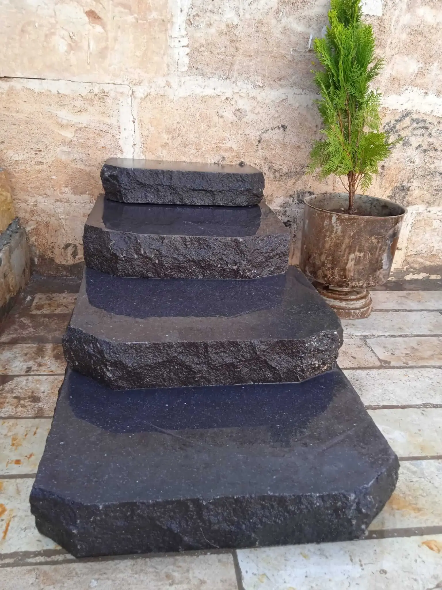 Dark, textured granite pavers stacked in ascending sizes against a stone wall, shown for are stone steps slippery.