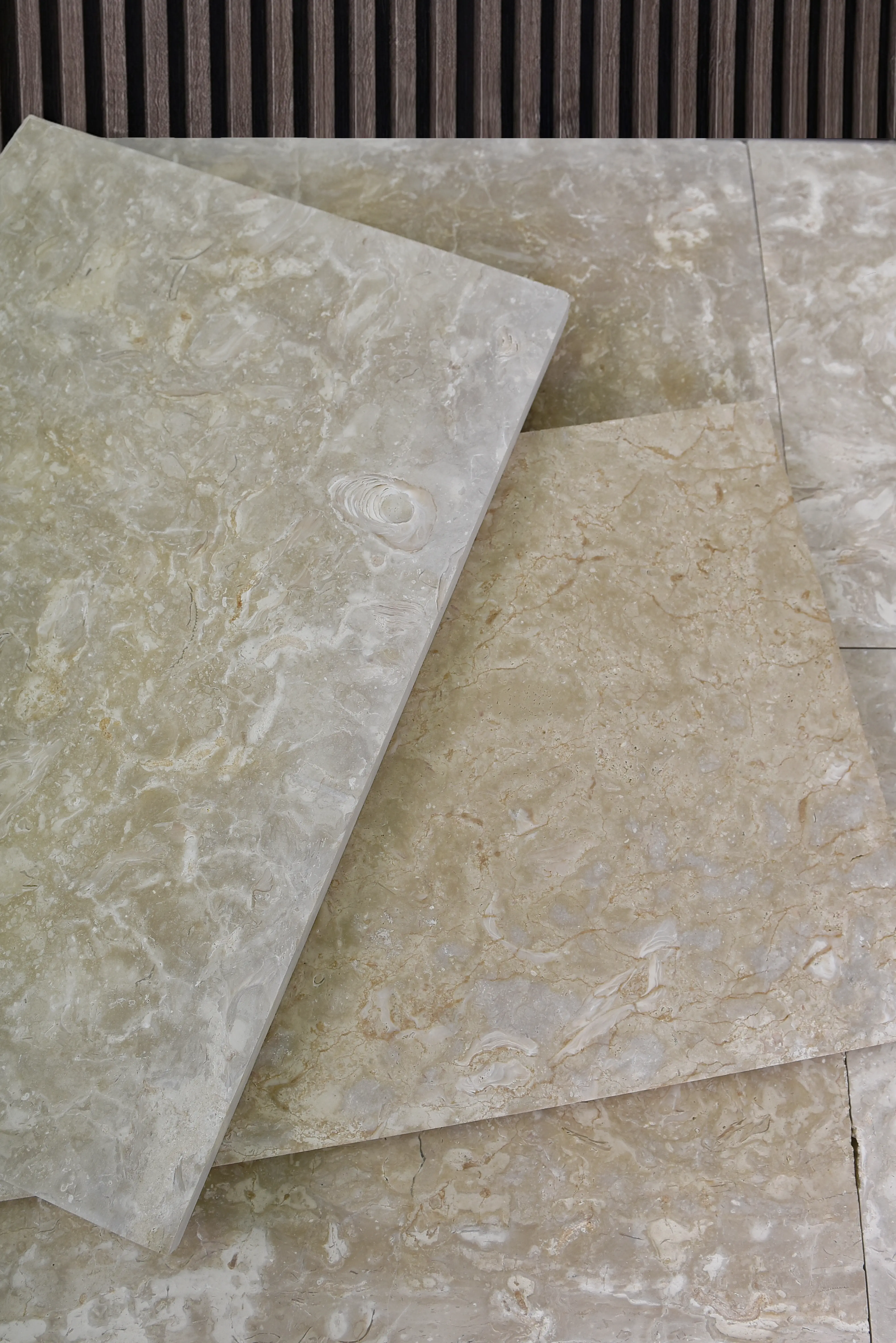 Close-up of textured light beige marble tiles with natural veining and fossil details, an example for black granite stone outdoor use.