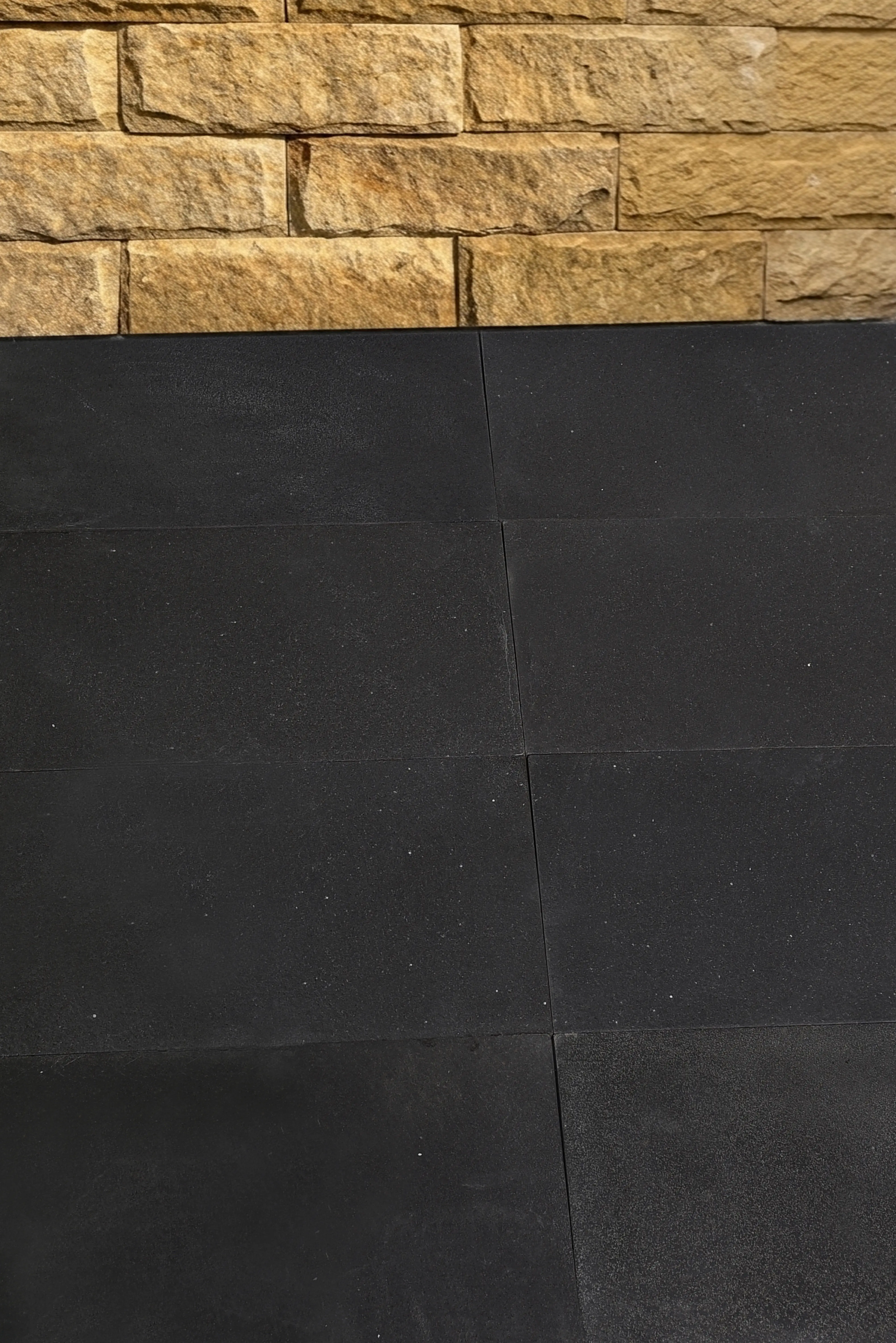 Close-up view of rough-hewn tan slate wall tiles above a textured black surface.