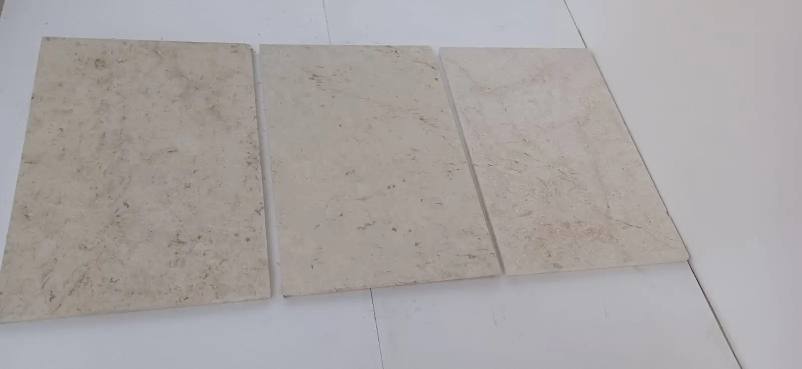 Close-up view of three beige limestone tiles with subtle marbling and texture, shown for white granite landscape rock.