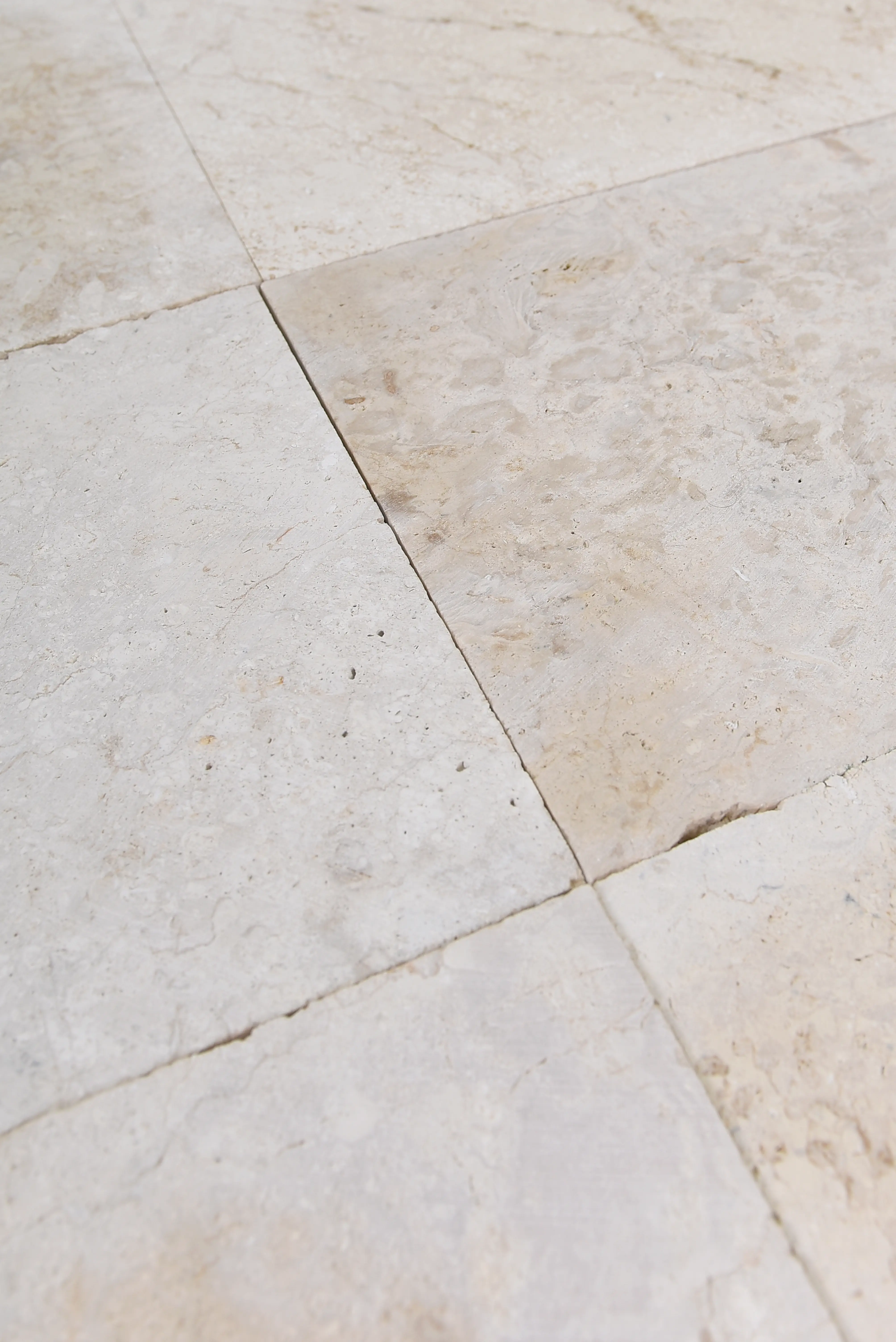 Close-up view of light travertine floor tiles showing natural texture and subtle color variations, a reference for pavers for garden beds.