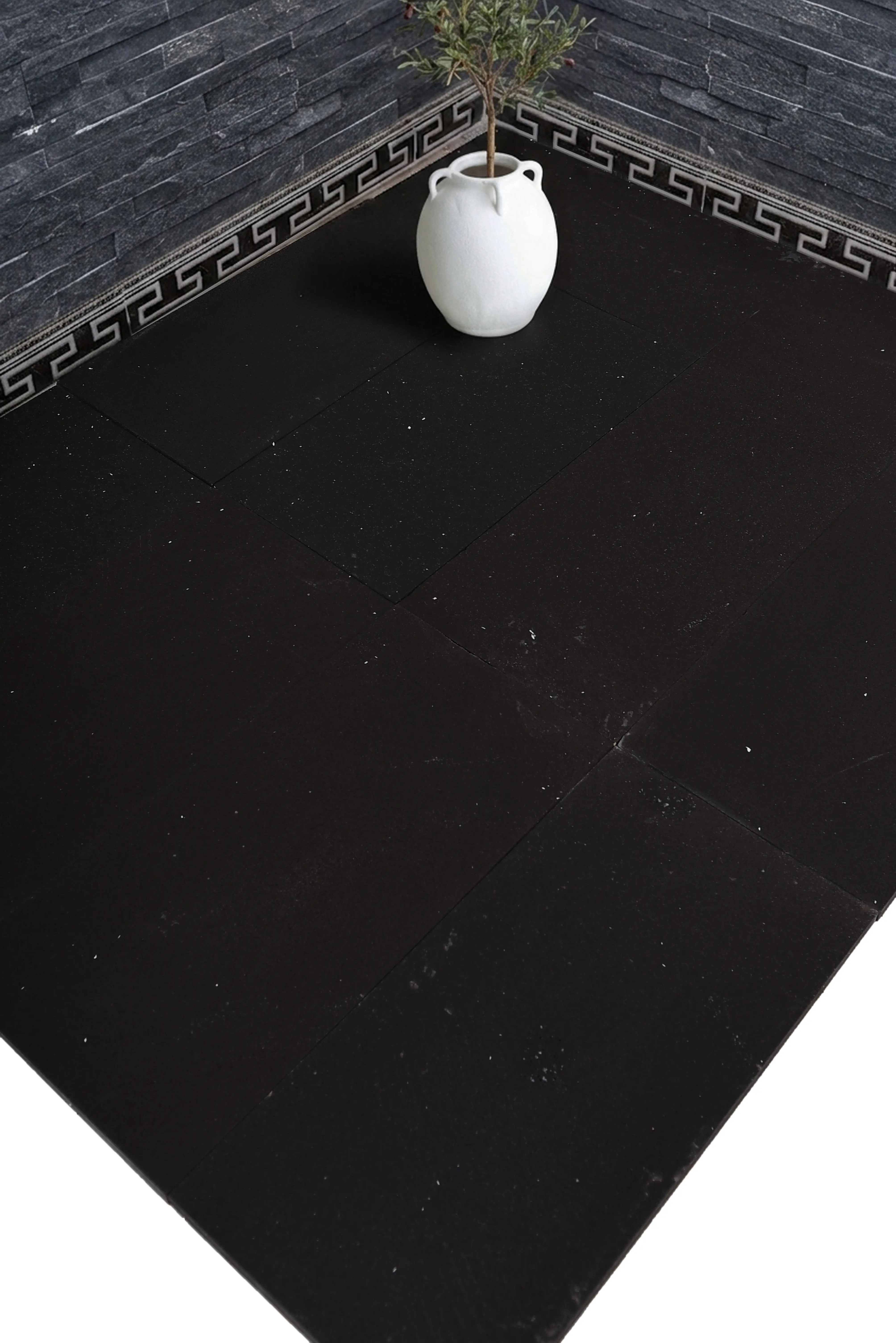 A white natural stone pot with a small plant sits on dark black floor tiles, an example for grey limestone care and cleaning.