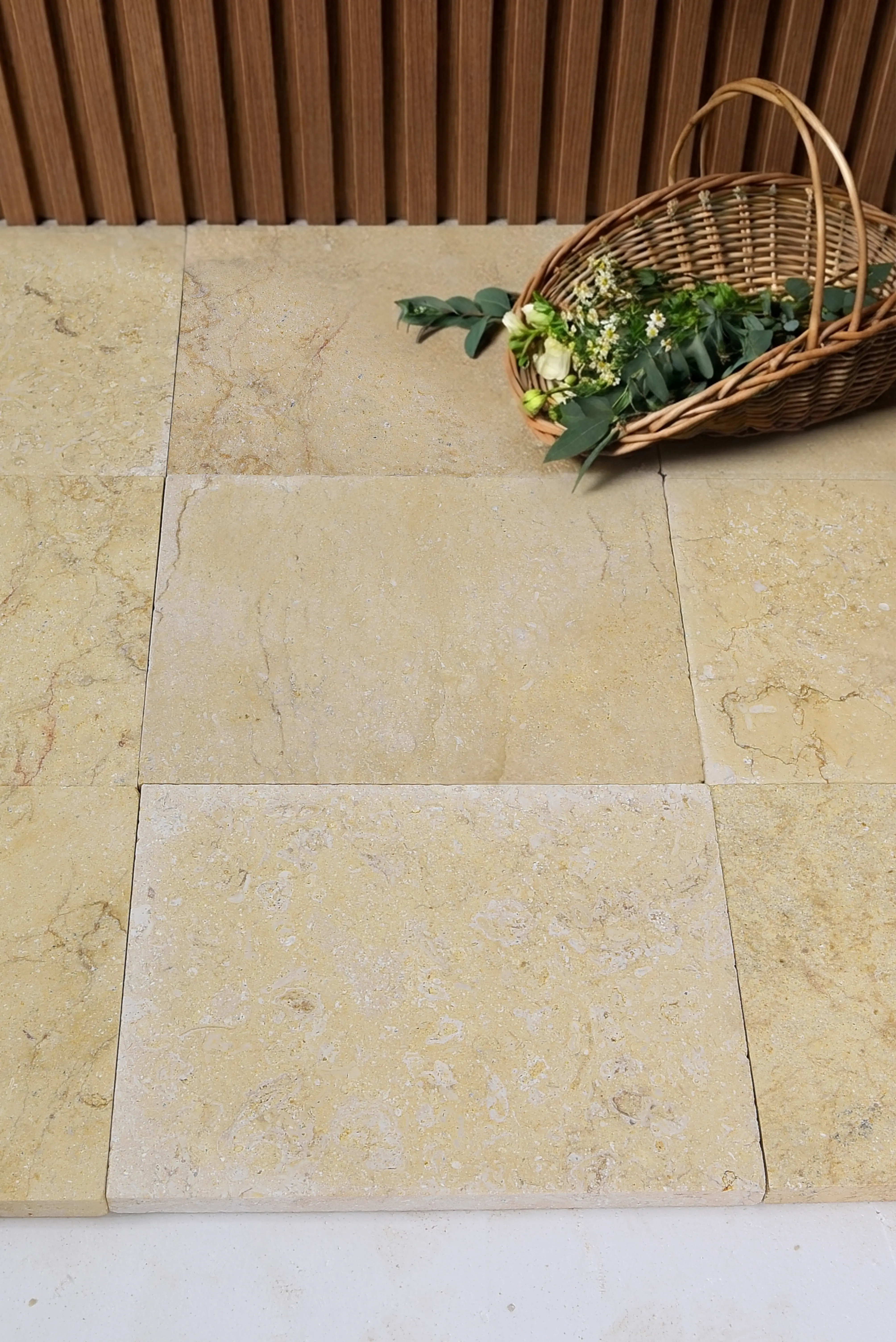Cream colored limestone pavers with a wicker basket and flowers on top, relevant to preparing ground for paving stones.