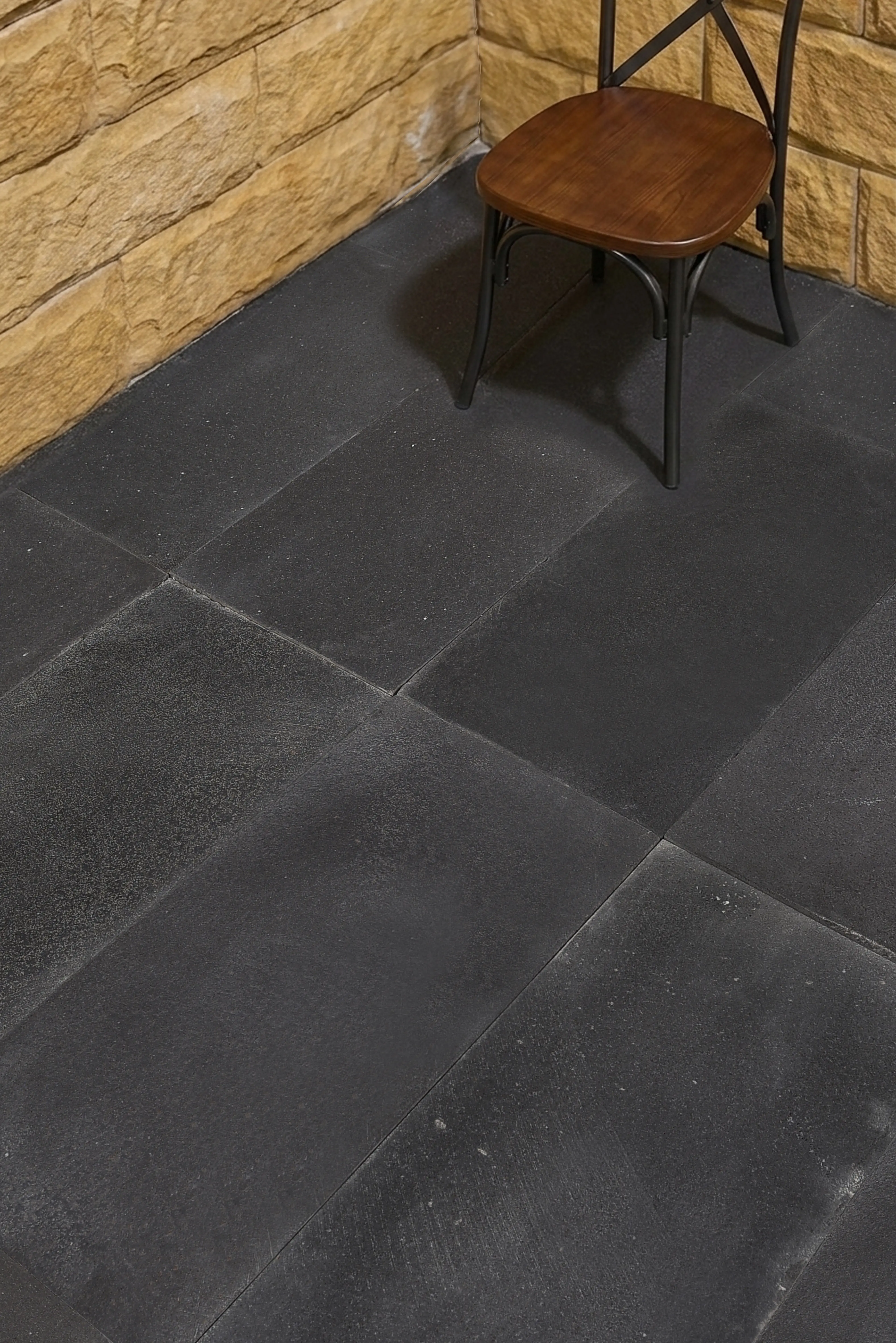 A wooden chair rests on a dark textured floor surface composed of large tiles, pictured for granite patio paver cost.