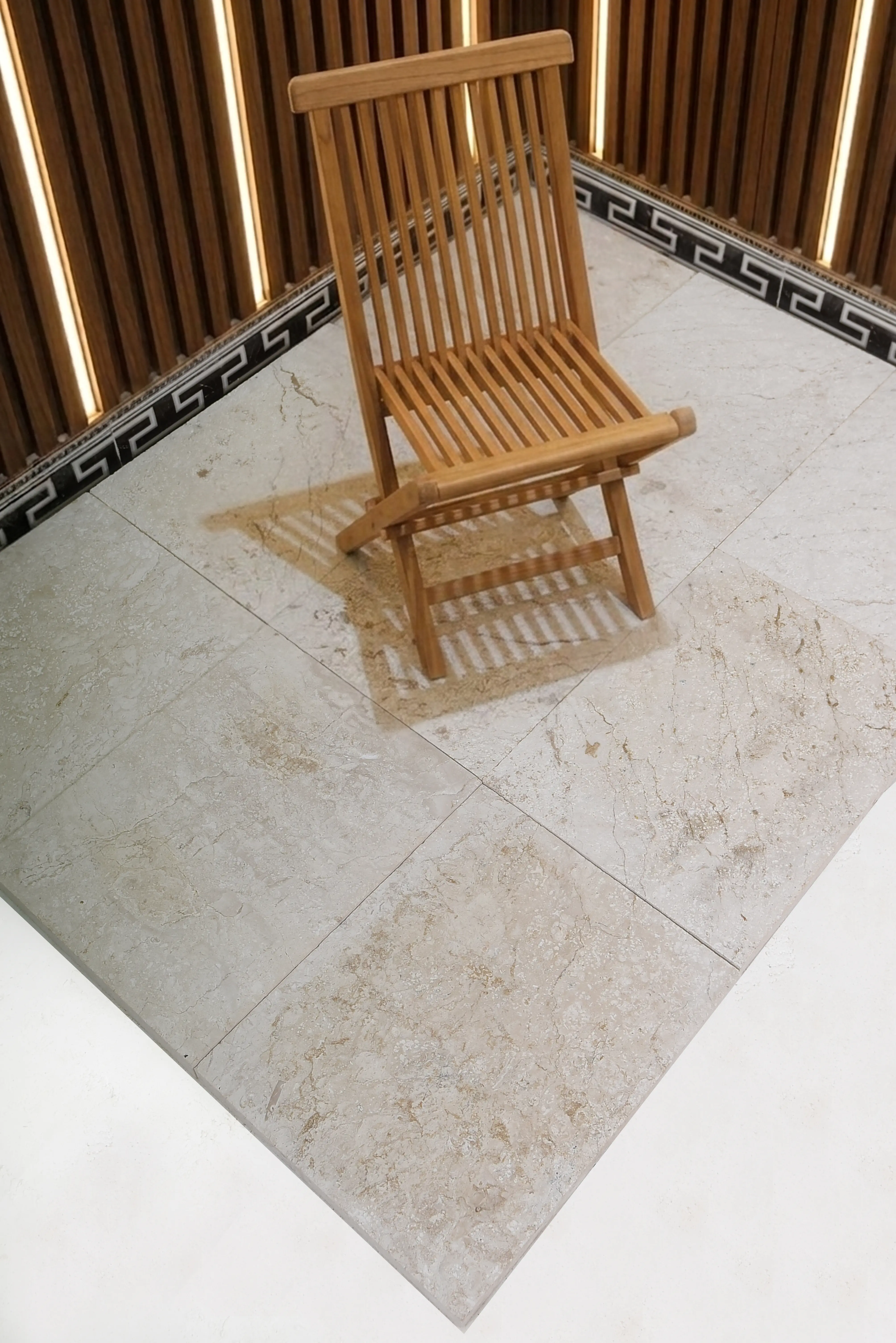 Wooden Chair on Marble Floor Light-colored travertine pavers laid in a grid pattern with a wooden chair casting shadows, shown for garden wall stones.
