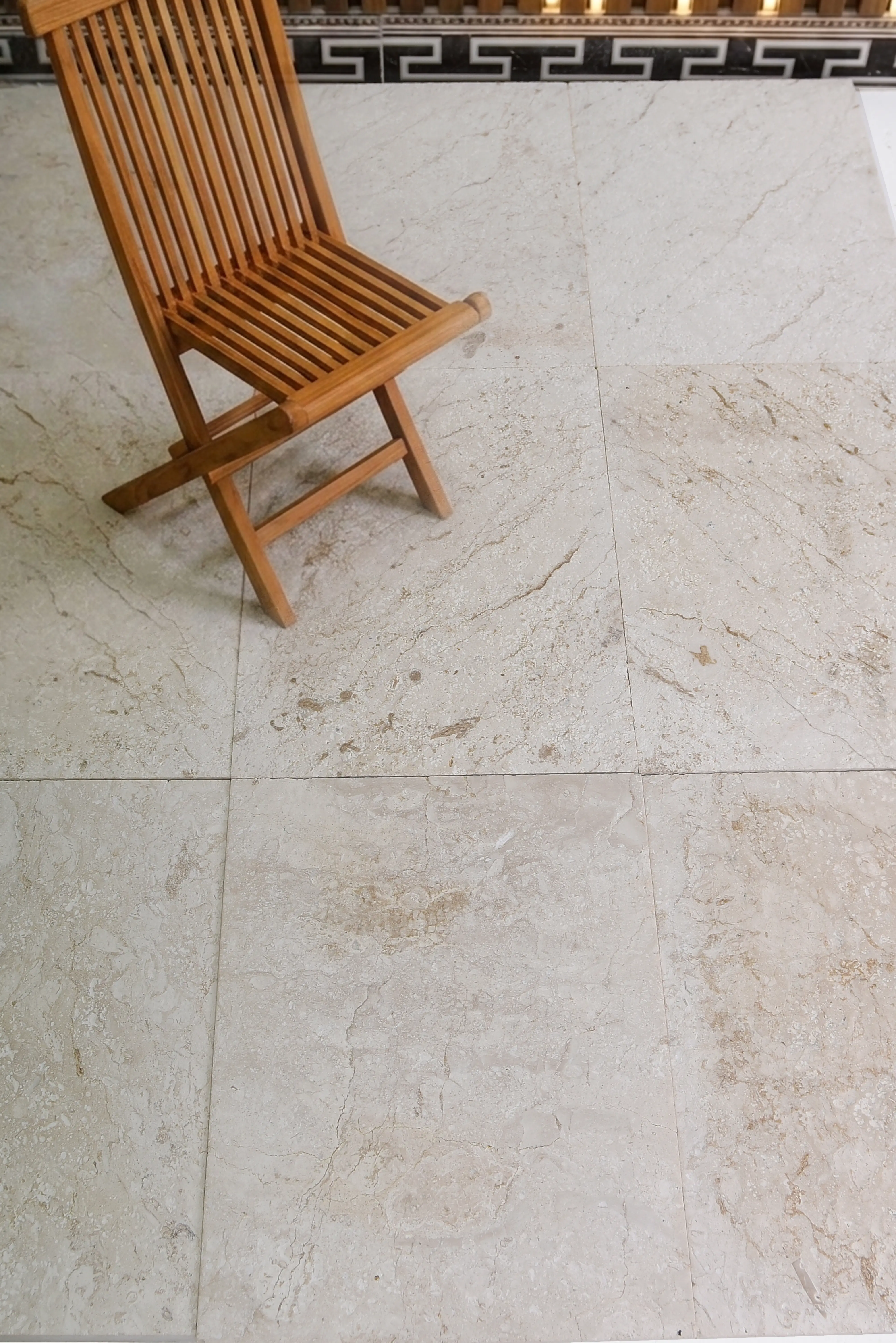 Wooden chair on light stone tiles A slatted wooden chair sits on a cream-colored travertine stone floor, relevant to stone kitchen floor tile ideas.