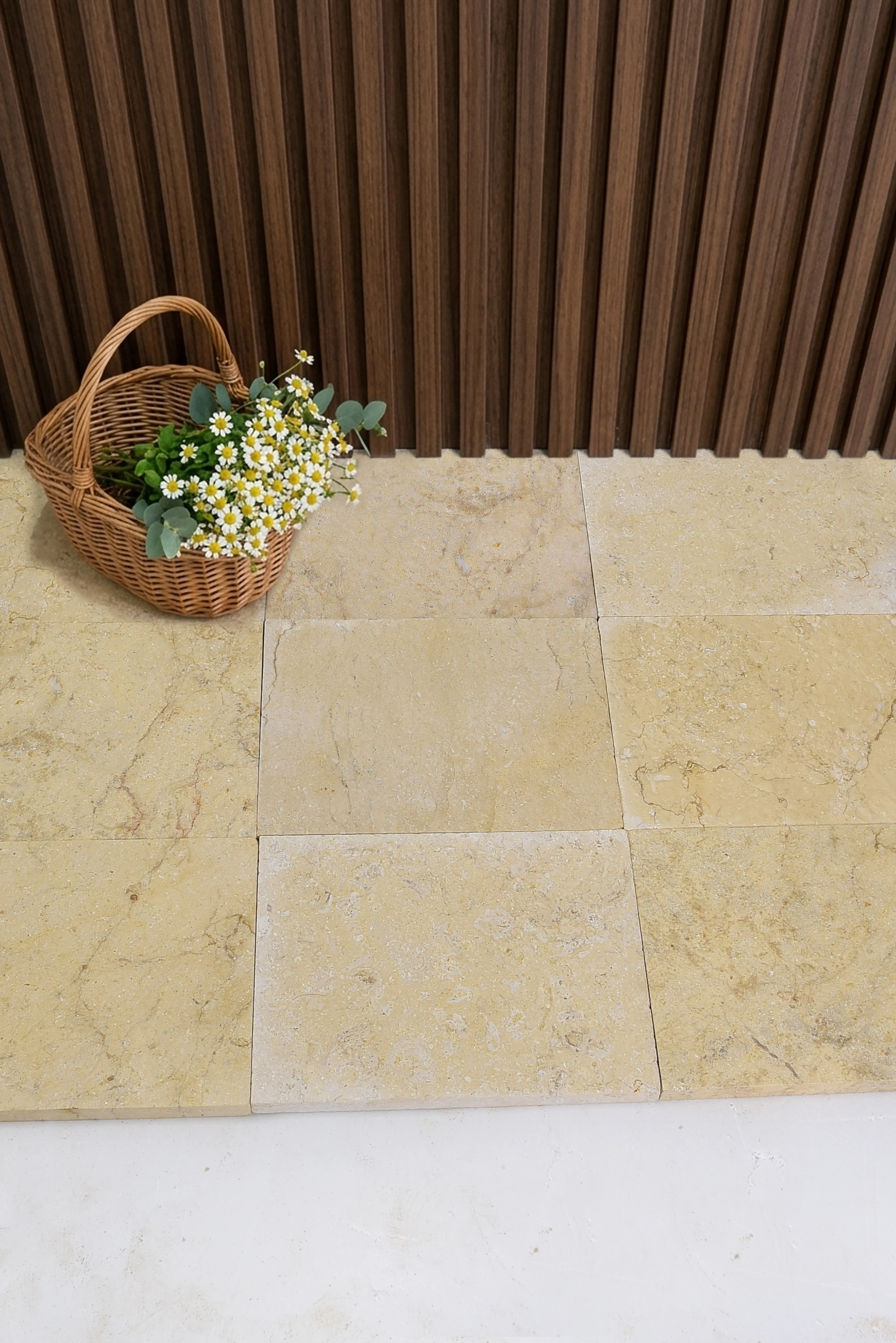 A woven basket filled with chamomile flowers and eucalyptus on travertine tiles, a reference for Stone Sills & Window Cills.