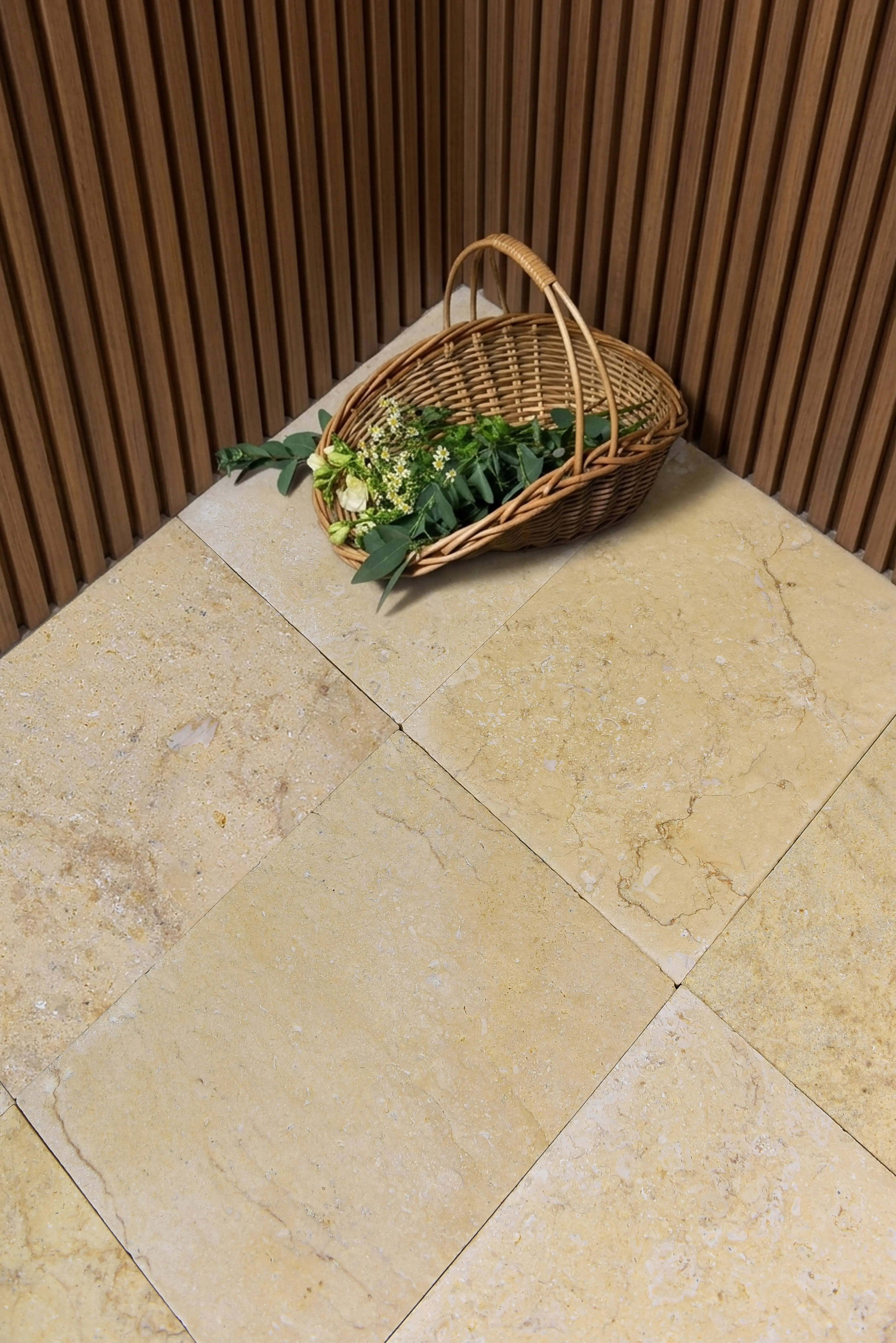 A woven basket filled with greenery and small flowers rests on light travertine floor tiles, a reference for paving stones for fire pit.