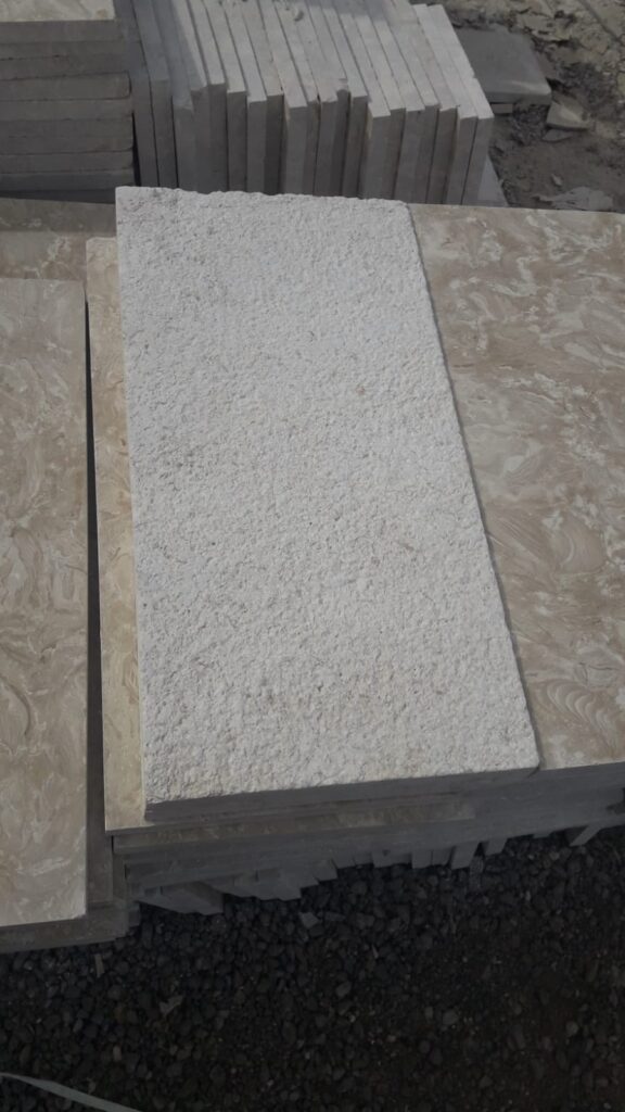Stacked bush-hammered white limestone slabs showing the pitted anti-slip face
