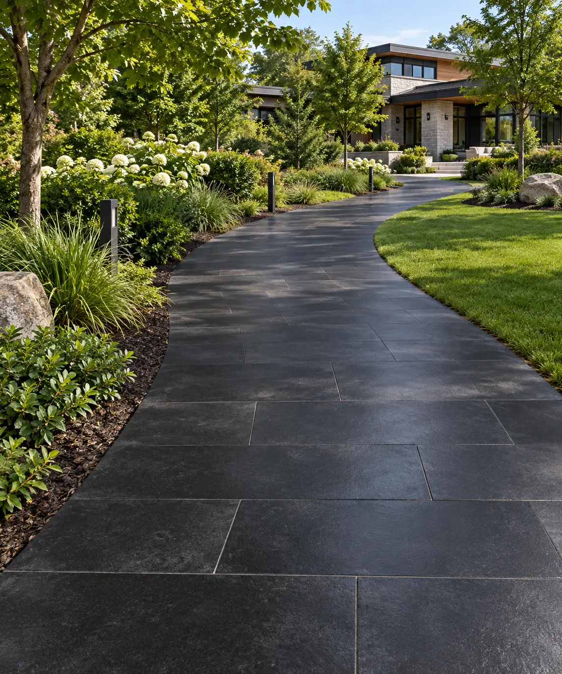 Curving Dark Paver Walkway in Lush Garden A winding walkway paved with dark basalt tiles leads through a vibrant, landscaped garden.
