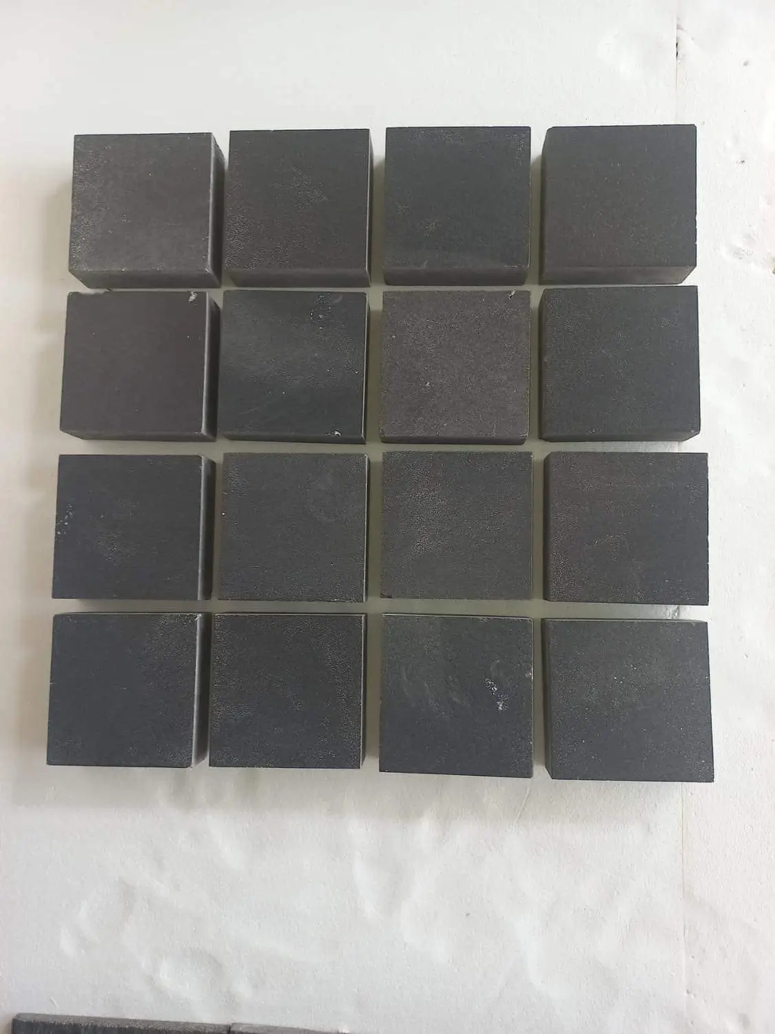 A grid of dark grey basalt cubes displayed on a white surface, a reference for edging pavers.