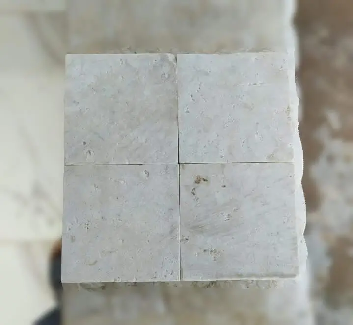 Four square, light beige cobblestone tiles arranged in a 2x2 grid showing natural texture, an example for cobblestone edging pavers.