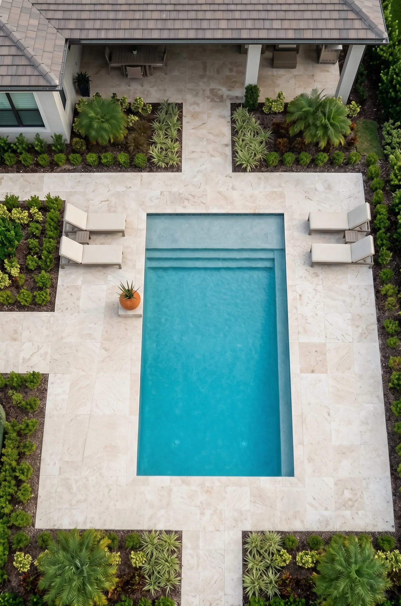 Luxury backyard with pool and lounge chairs Travertine pavers surrounding a bright blue swimming pool with built-in steps and lounge chairs.