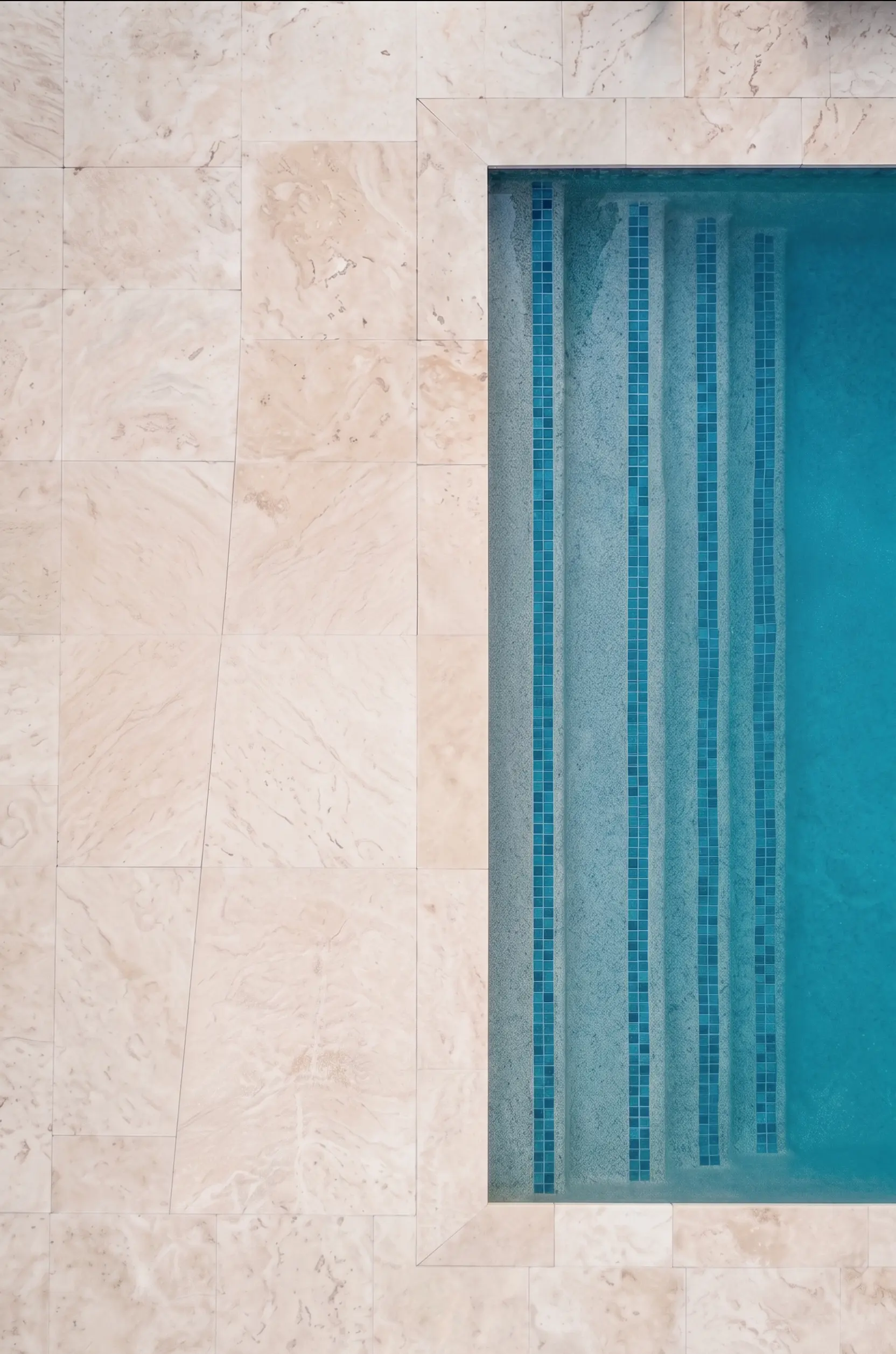 Pool Steps with Tile Accent A detailed view of travertine pool coping leading to blue tiled steps, shown for how thick are travertine pavers.