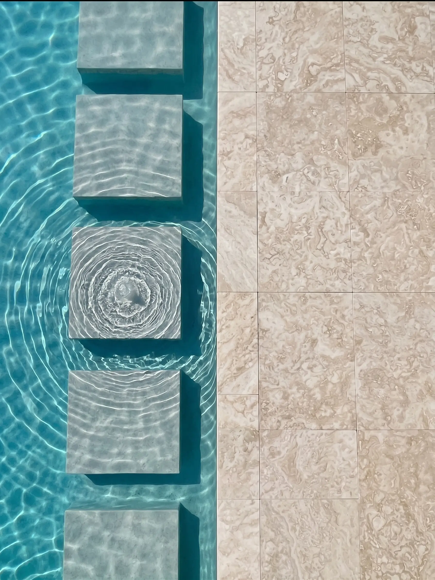 Poolside Marble Pavers and Water Feature Light marble pavers contrast with a refreshing blue pool featuring stepping stones.