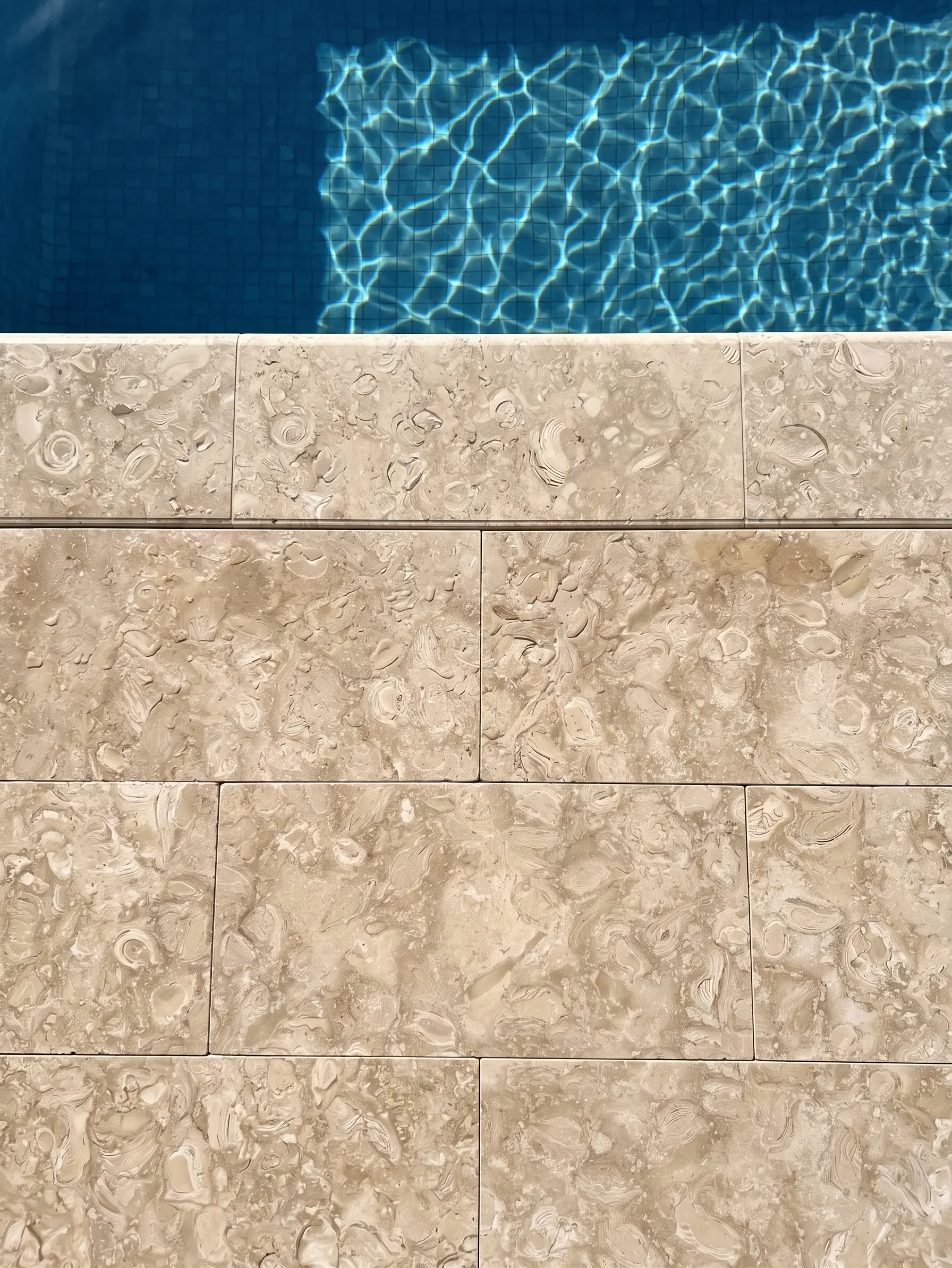 Close-up of tan travertine coping tiles adjacent to a blue pool surface, a reference for 30mm travertine pavers.