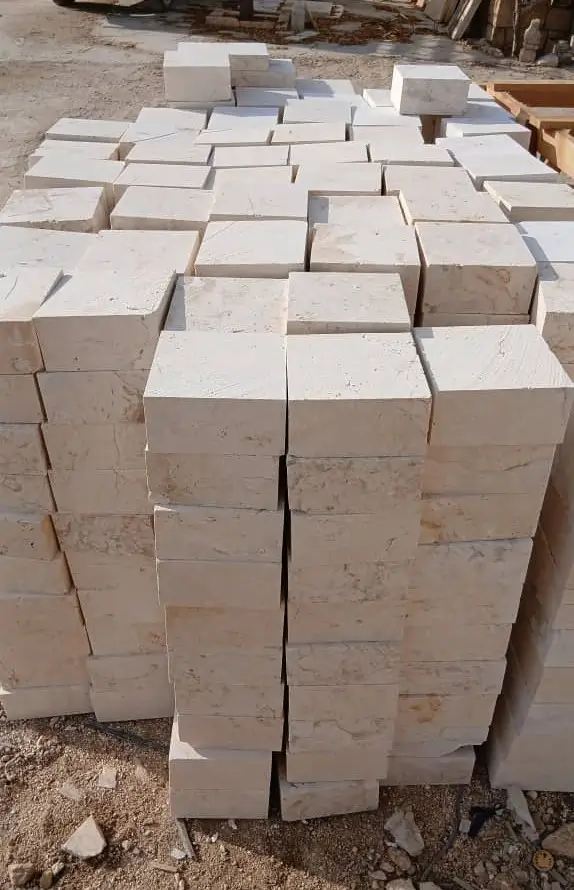 Neatly stacked beige cobblestone blocks form a textured outdoor construction material display, pictured for belgian cobblestone pavers.