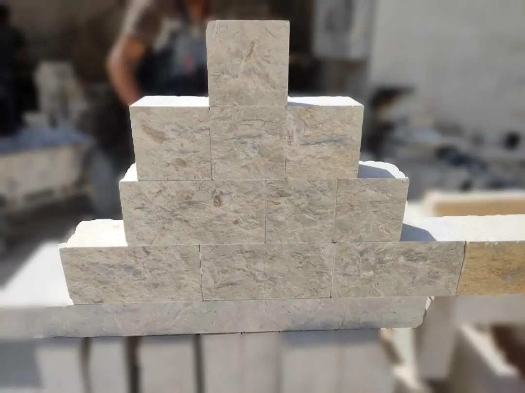 Stacked beige cobblestone blocks forming a stepped pyramid shape outdoors, pictured for thin cobblestone pavers explained.