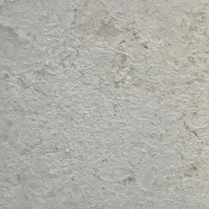 Macro view of a brushed limestone paver surface with fine sandy grain, scattered brown patches and small dark specks