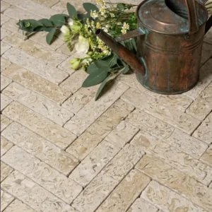 Cream cobblestone pavers in a herringbone pattern styled with a copper watering can and flowers