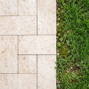 Cream travertine cobblestones in a modular pattern bordering a grass and sedum edge